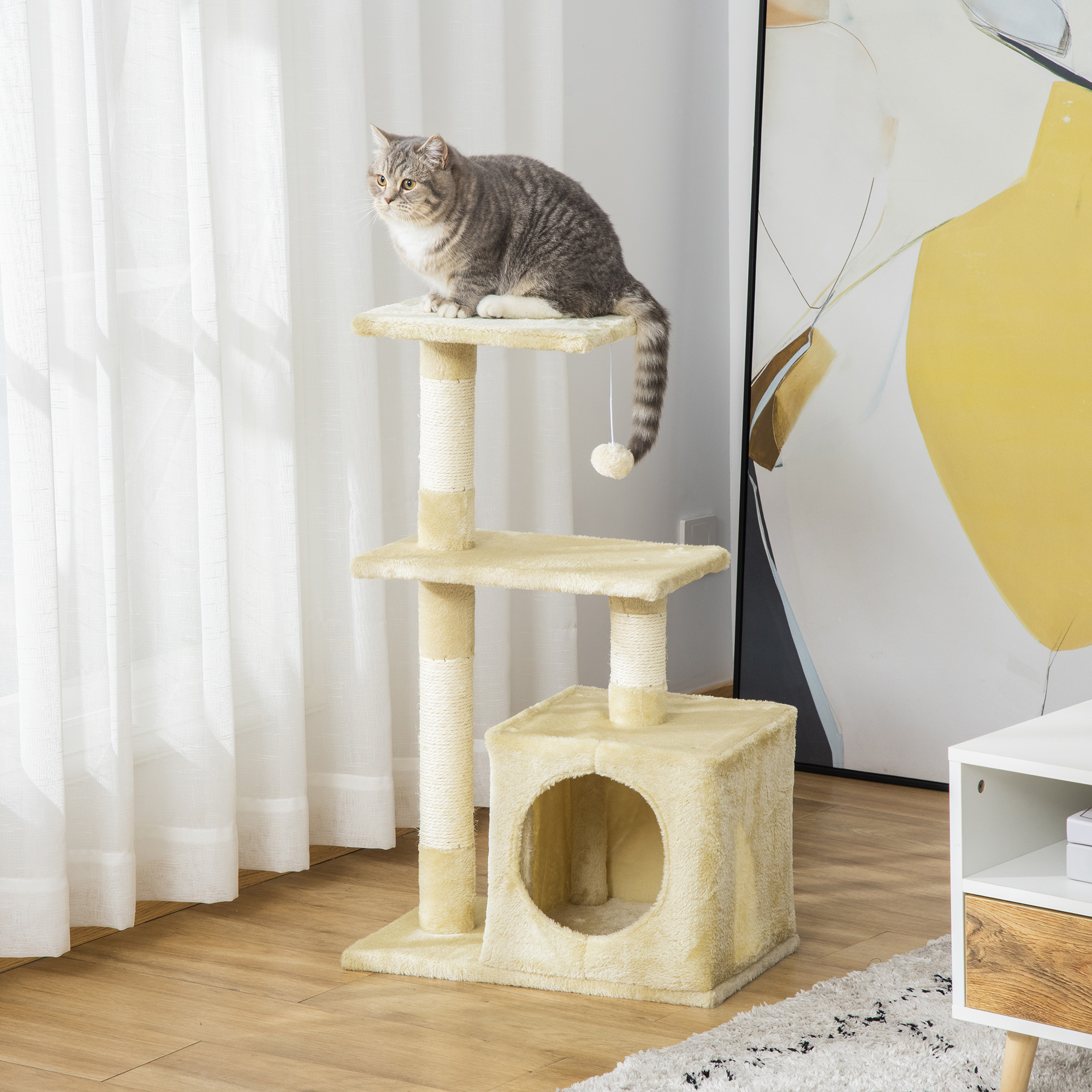 Un gatto tigrato grigio e bianco siede sulla piattaforma superiore di un tiragraffi beige chiaro in una stanza luminosa.