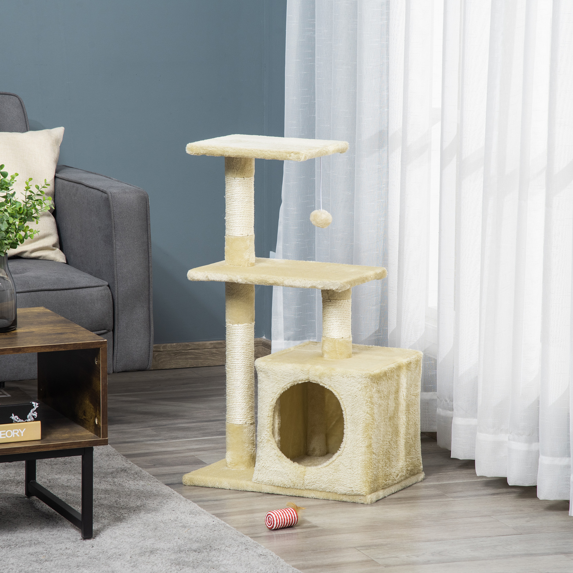 Un albero per gatti beige con piattaforme, tiragraffi e una cuccia si trova su un pavimento in legno in salotto.
