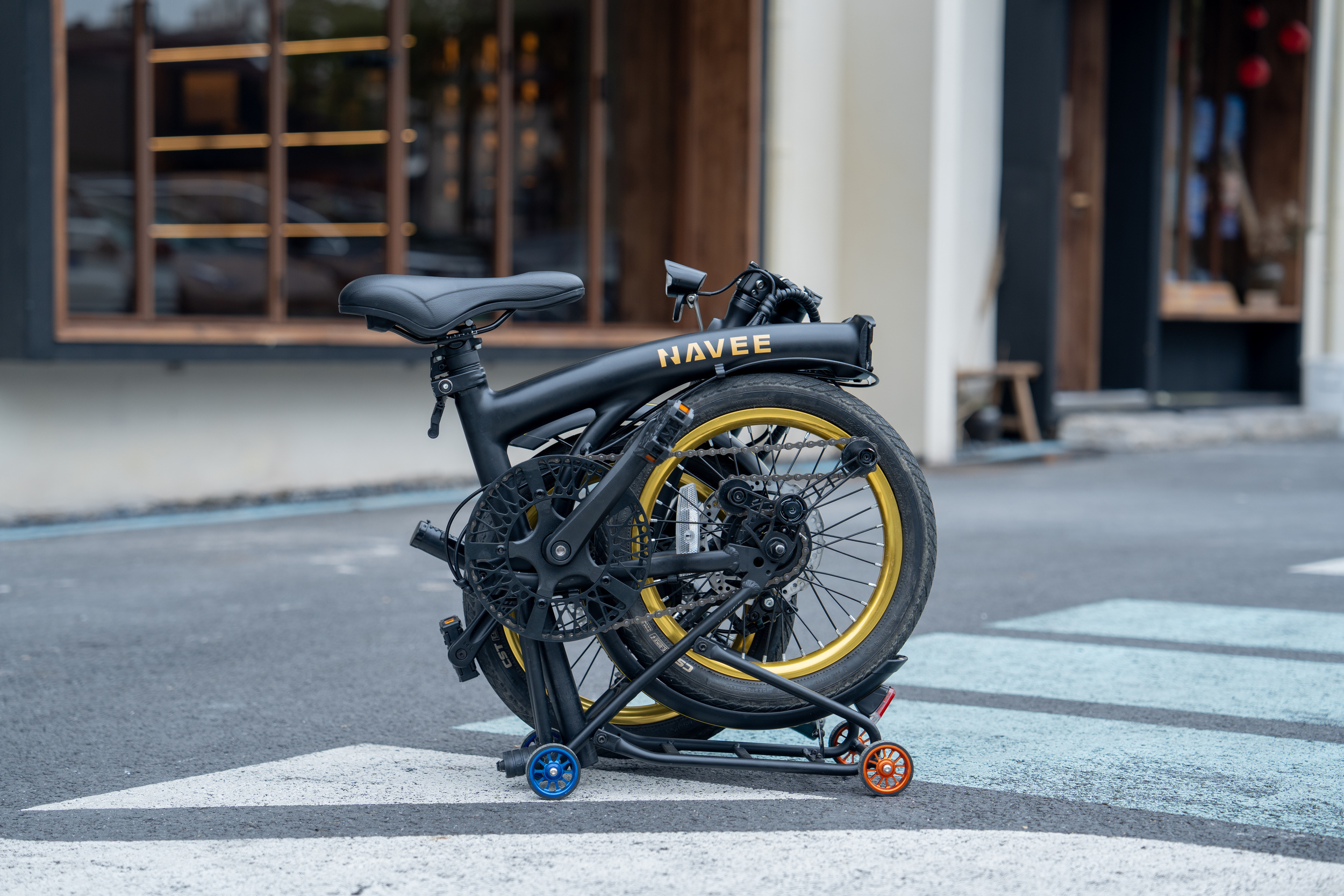 Una bicicletta elettrica nera piegata con cerchi dorati e il marchio Navee si trova sulla strada.