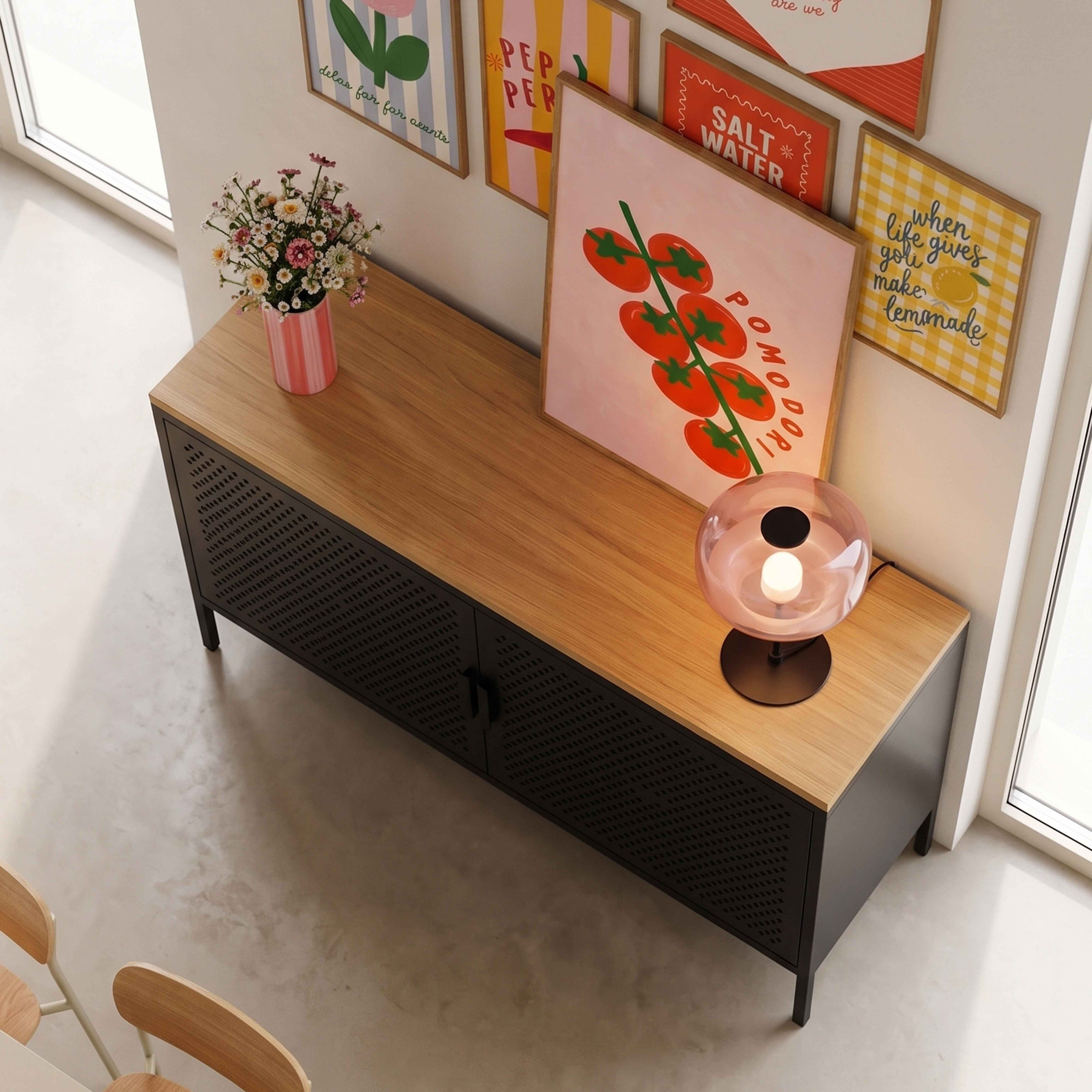 Ein Holzsideboard mit schwarzem Metallgestell, verziert mit gerahmten Postern, Blumen und einer Glaskugel-Lampe.