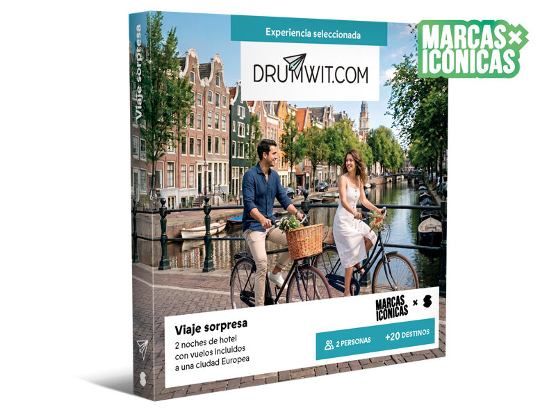 Una pareja pasea en bicicleta junto a un canal europeo con edificios históricos al fondo.