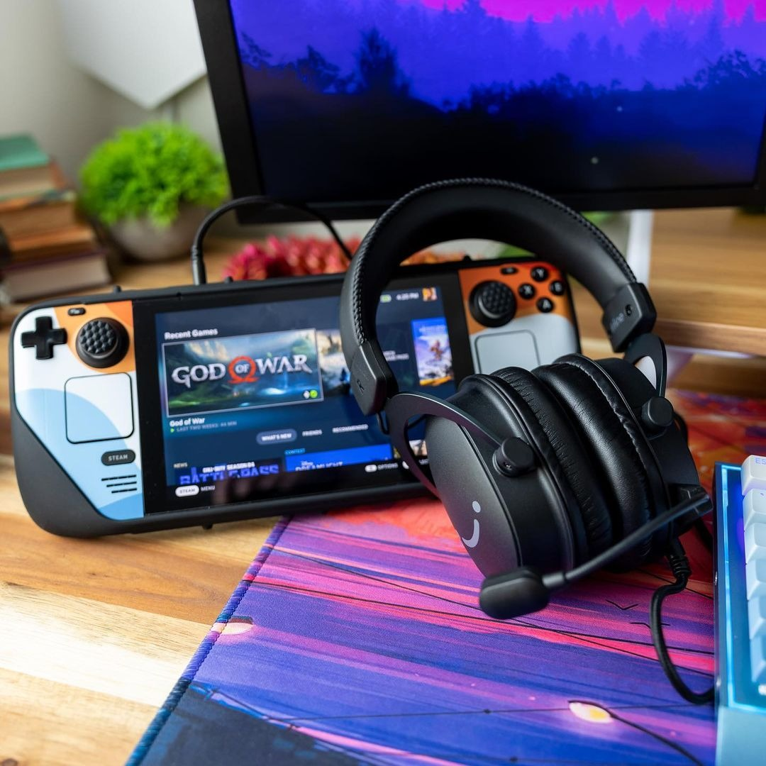 Cuffie nere con microfono sono poggiate su una scrivania davanti a una console portatile e a un monitor.