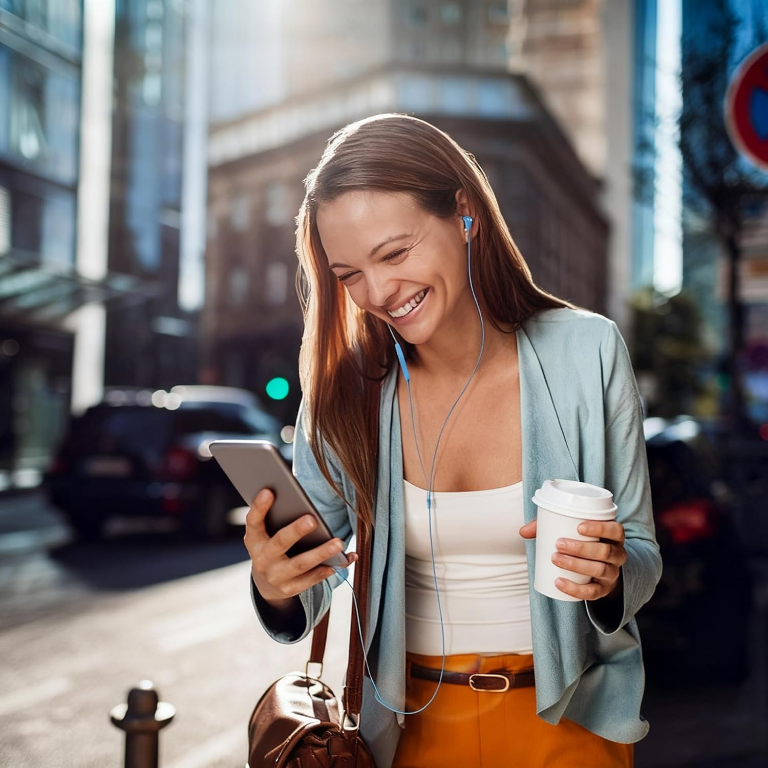 Eine lächelnde Frau geht durch eine Stadtstraße, hört Musik auf ihrem Handy und hält einen Kaffeebecher.