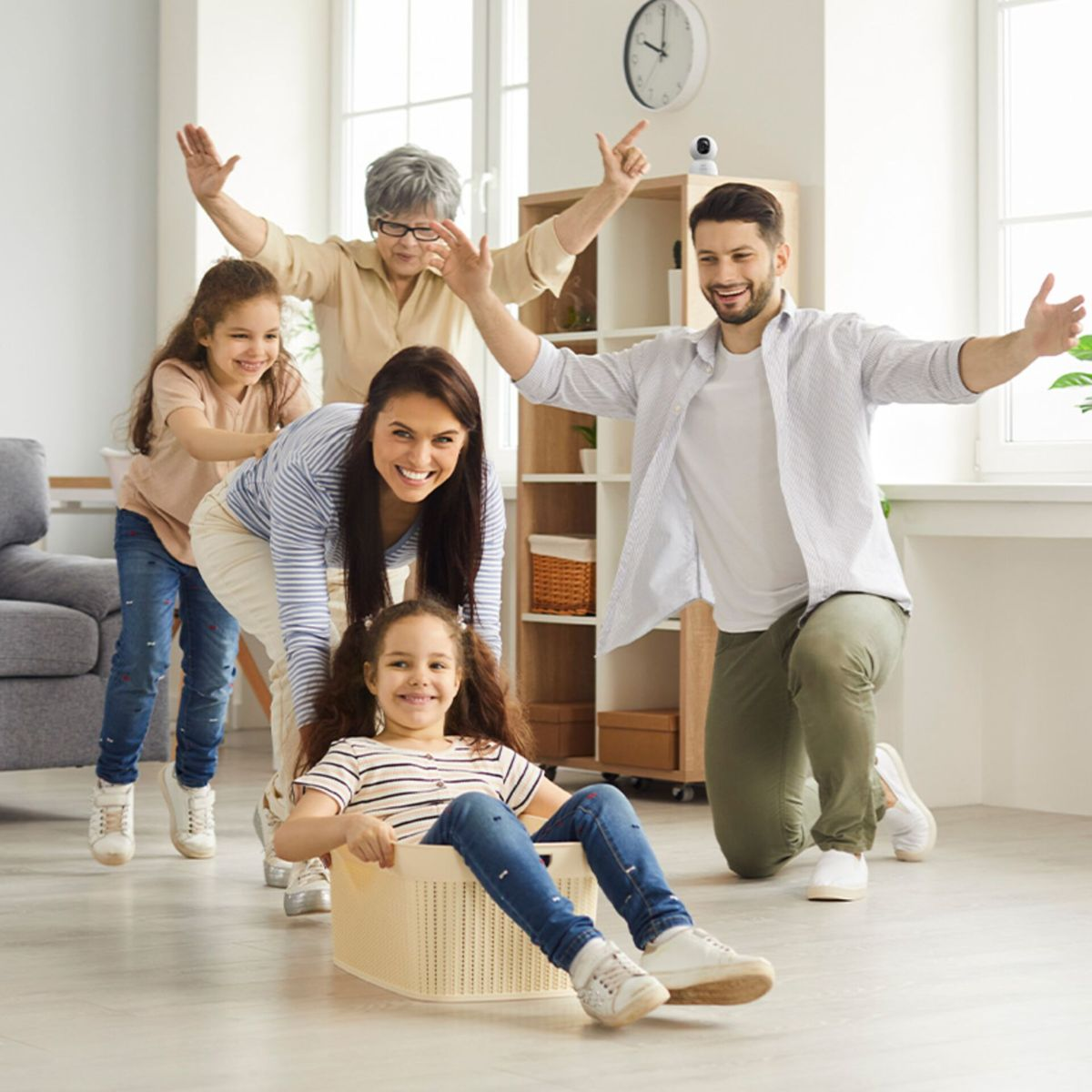 Eine glückliche Familie spielt zusammen in einem hellen Wohnzimmer, während ein Kind in einem Korb sitzt.