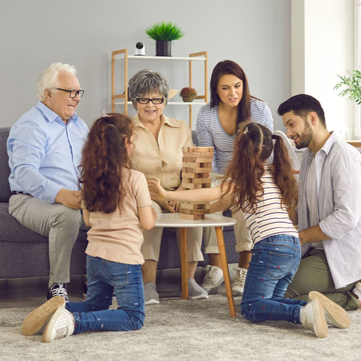 Una famiglia multigenerazionale gioca felicemente con i blocchi di legno sul pavimento del soggiorno.