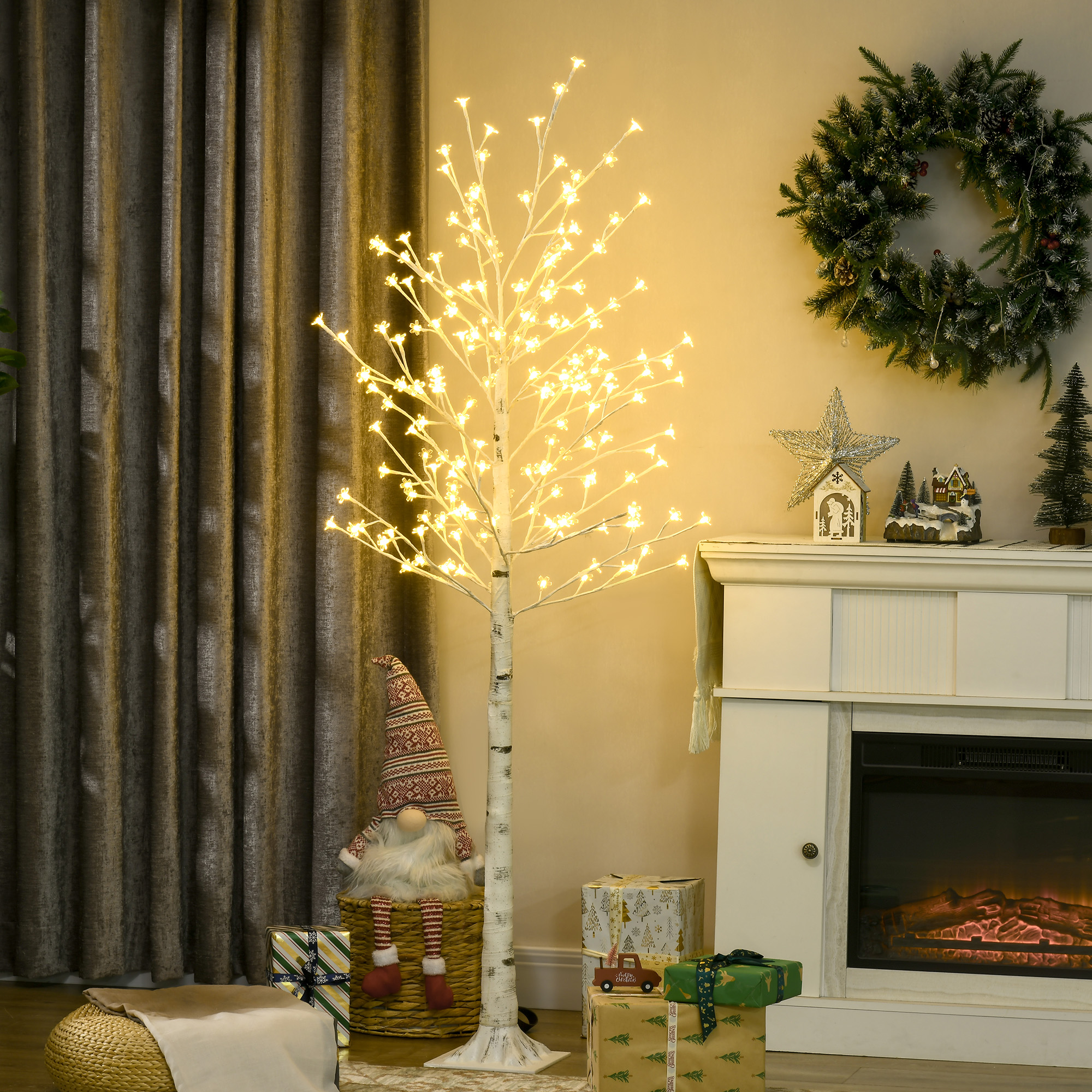 Árbol artificial iluminado con regalos, chimenea y decoración navideña en una sala.