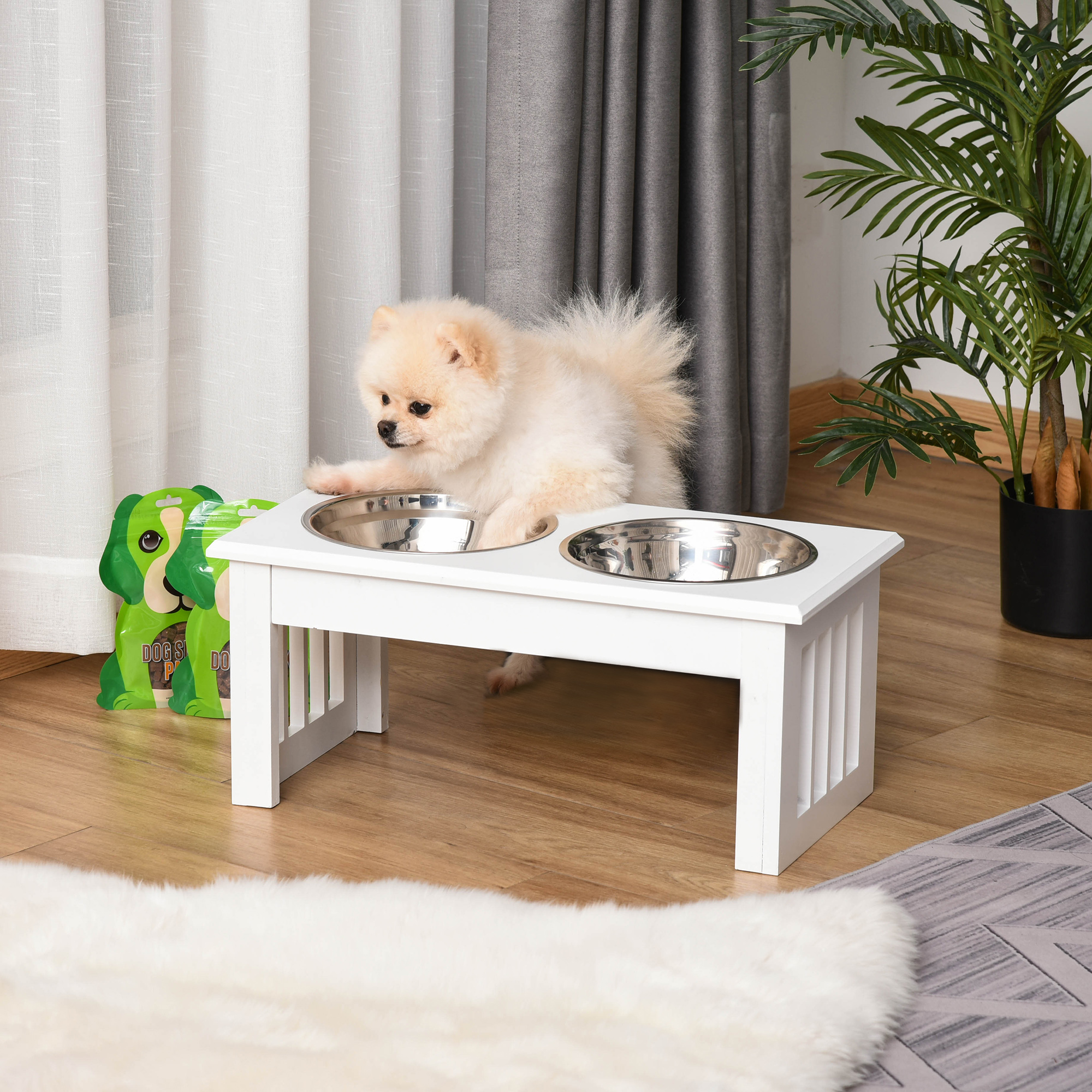 Un soffice volpino di Pomerania chiaro si trova su una mangiatoia bianca rialzata con due ciotole in una stanza.