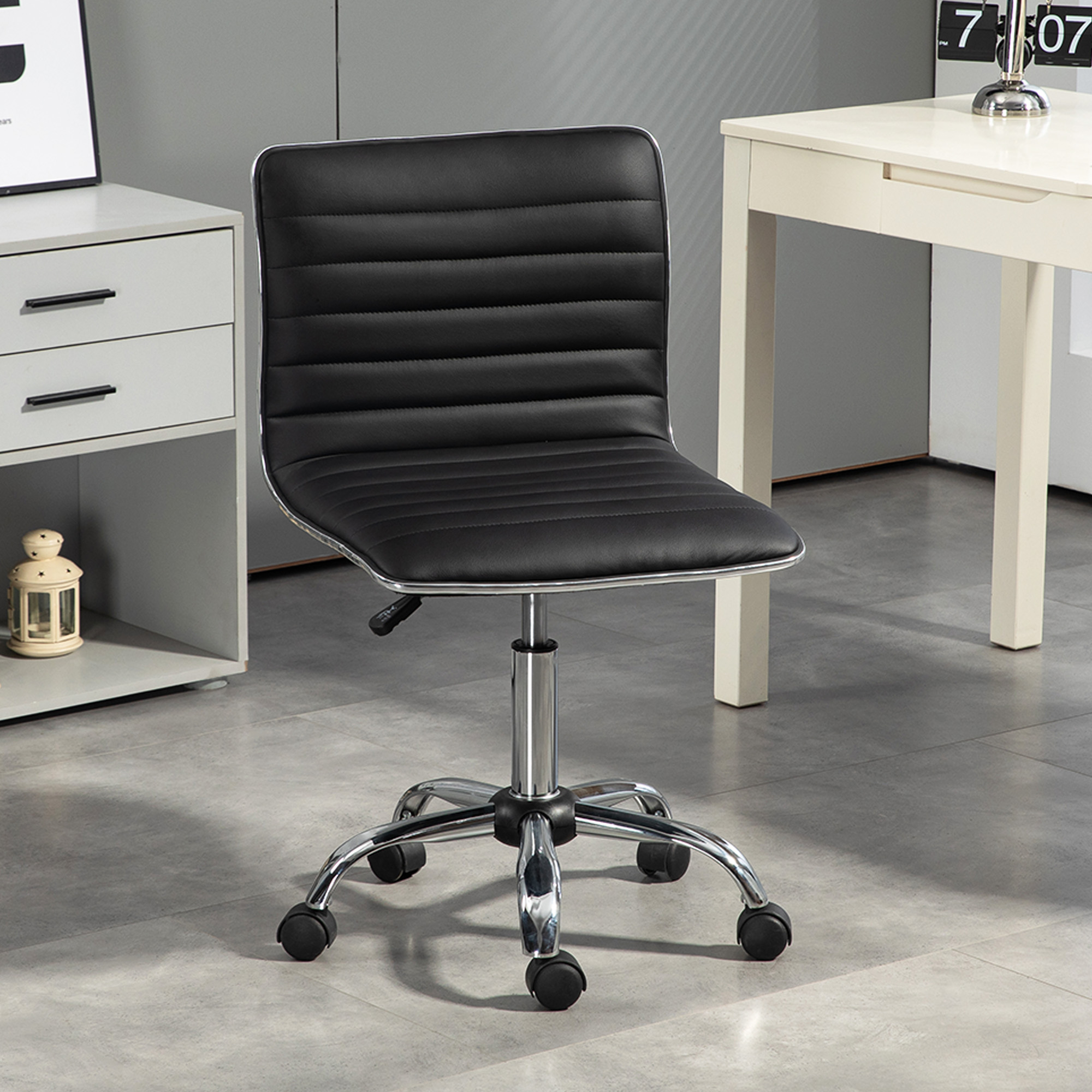 Una sedia da ufficio in pelle nera con base cromata si trova su un pavimento piastrellato grigio in una stanza moderna con una scrivania bianca.