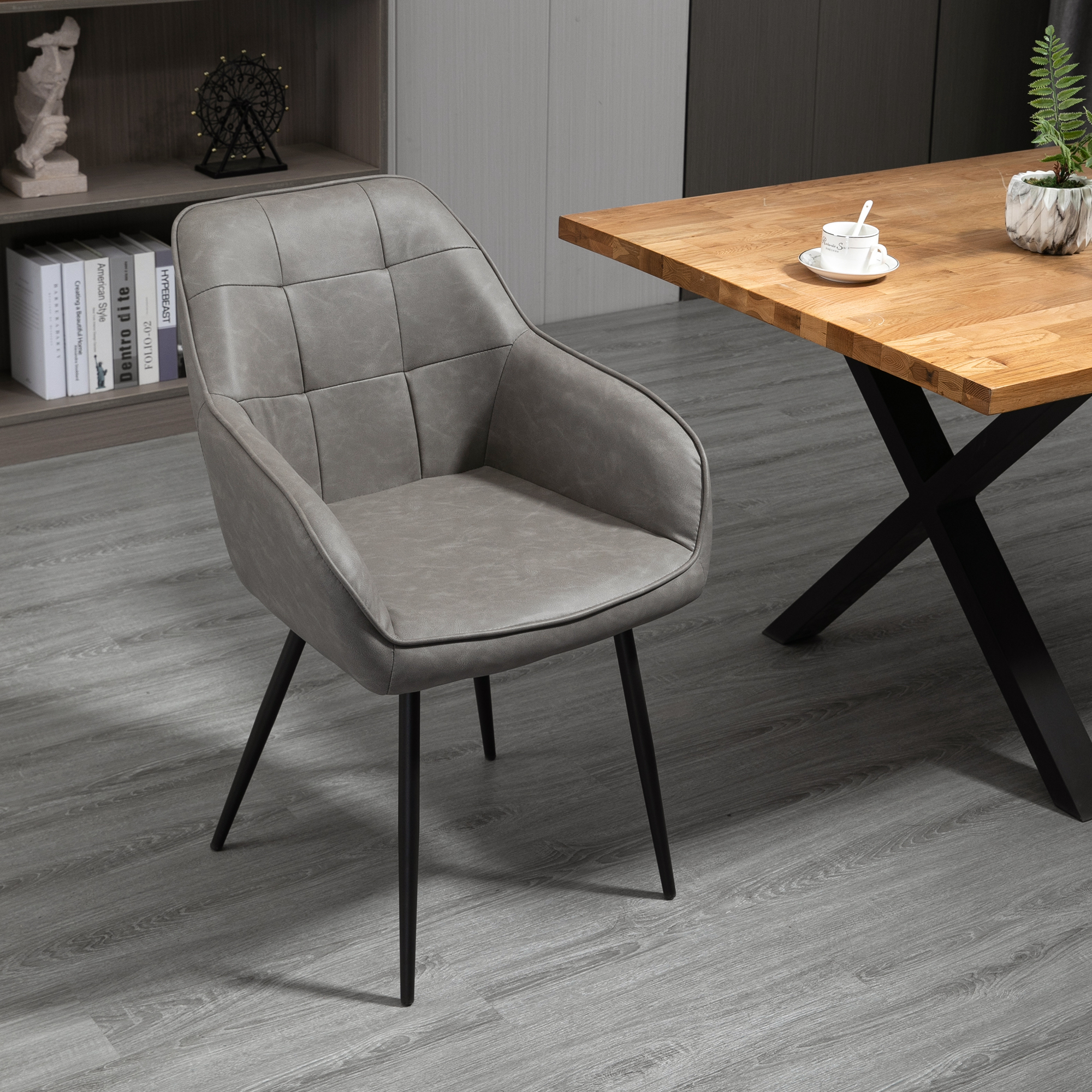 Una sedia imbottita grigia con gambe in metallo nero accanto a un tavolo di legno in una sala da pranzo.