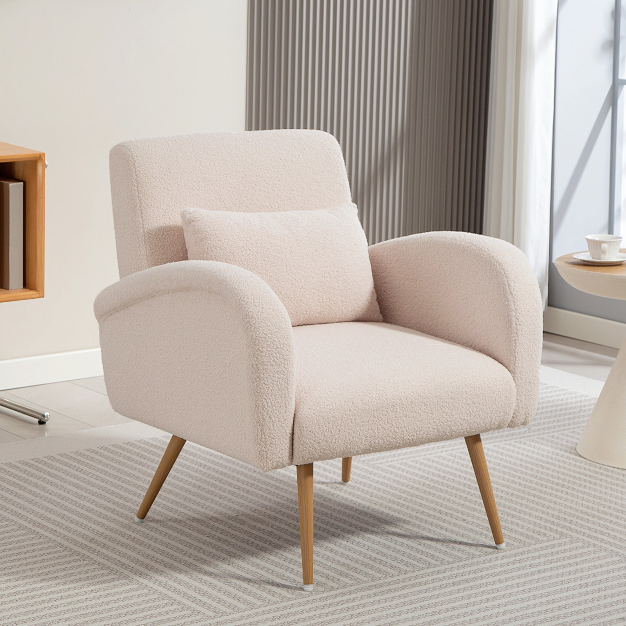Poltrona in tessuto teddy beige con cuscino su tappeto fantasia vicino a parete chiara.