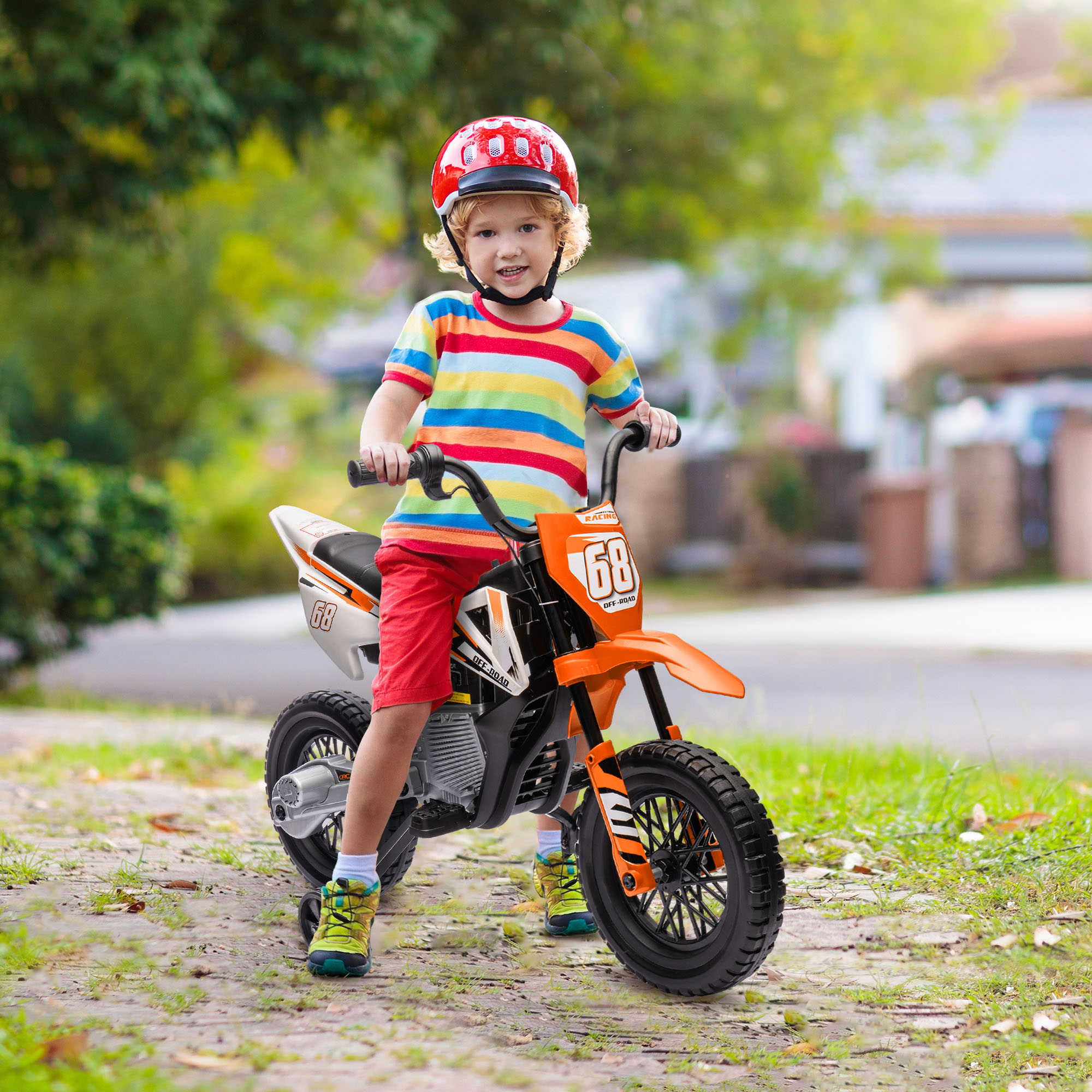 Un bambino con casco rosso e maglietta a righe siede su una piccola moto arancione all'aperto.