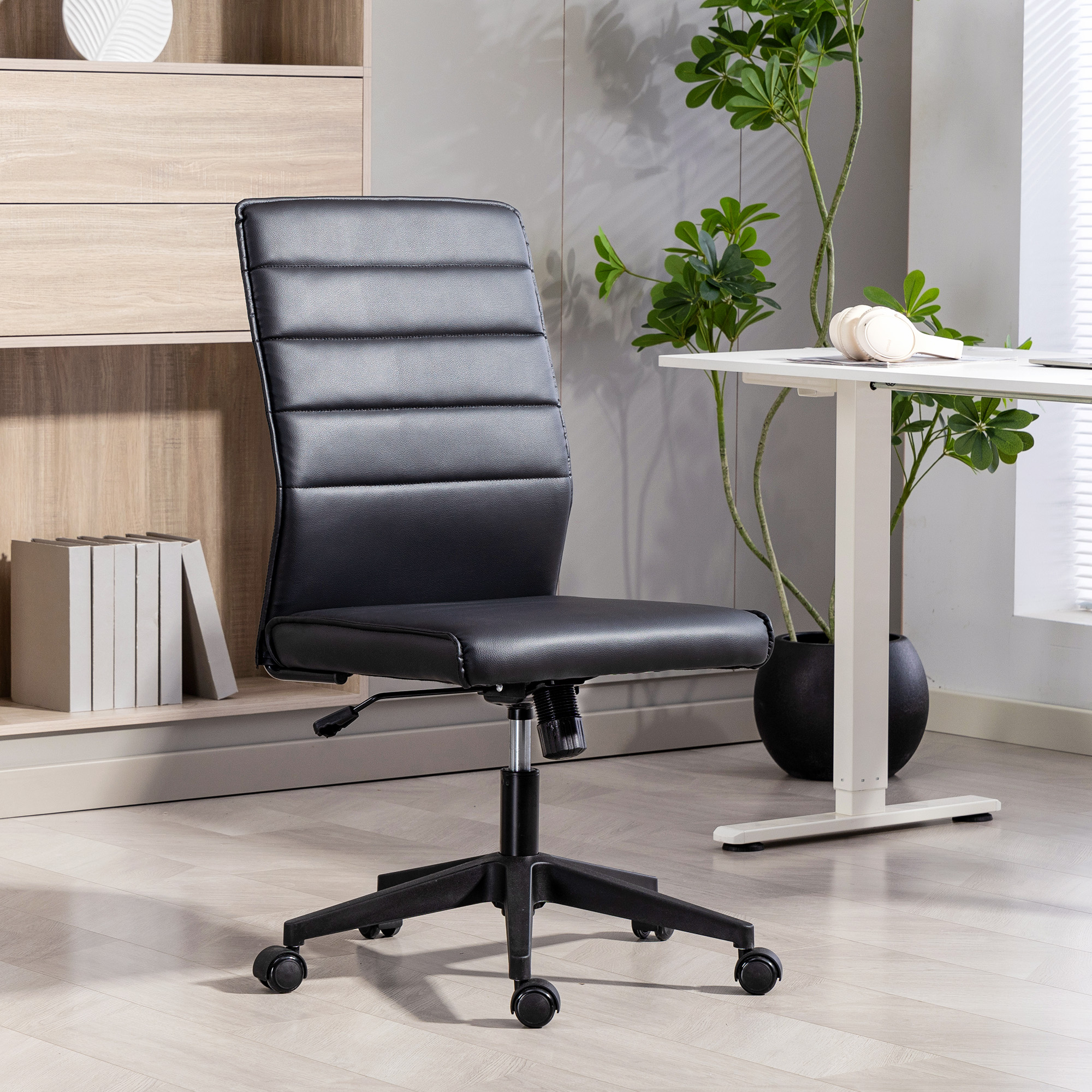 Una sedia da ufficio in pelle nera con ruote, scrivania bianca e pianta in vaso.