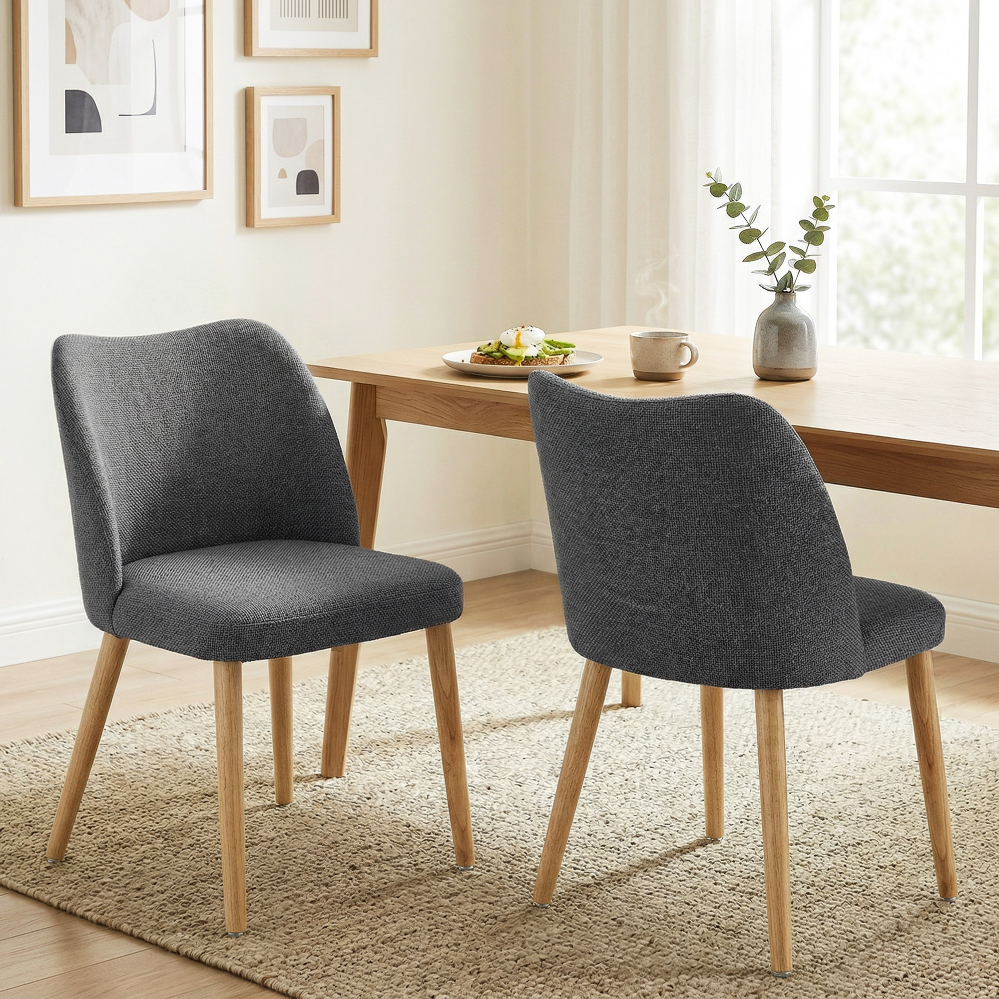 Due sedie da pranzo in tessuto grigio scuro con gambe in legno su un tappeto beige.