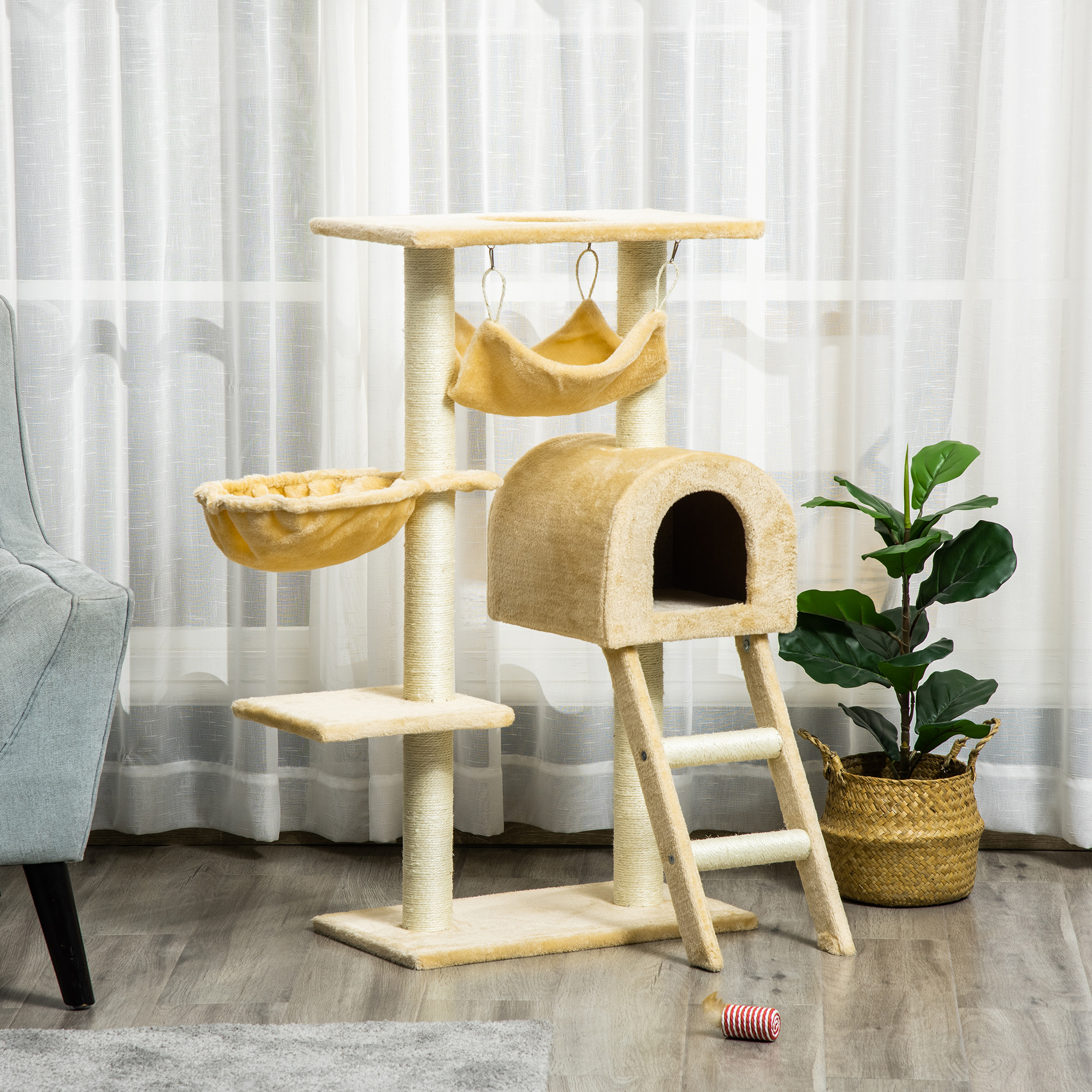 Albero per gatti beige con amaca, cuccia e scala, davanti a tende e accanto a una pianta in vaso.