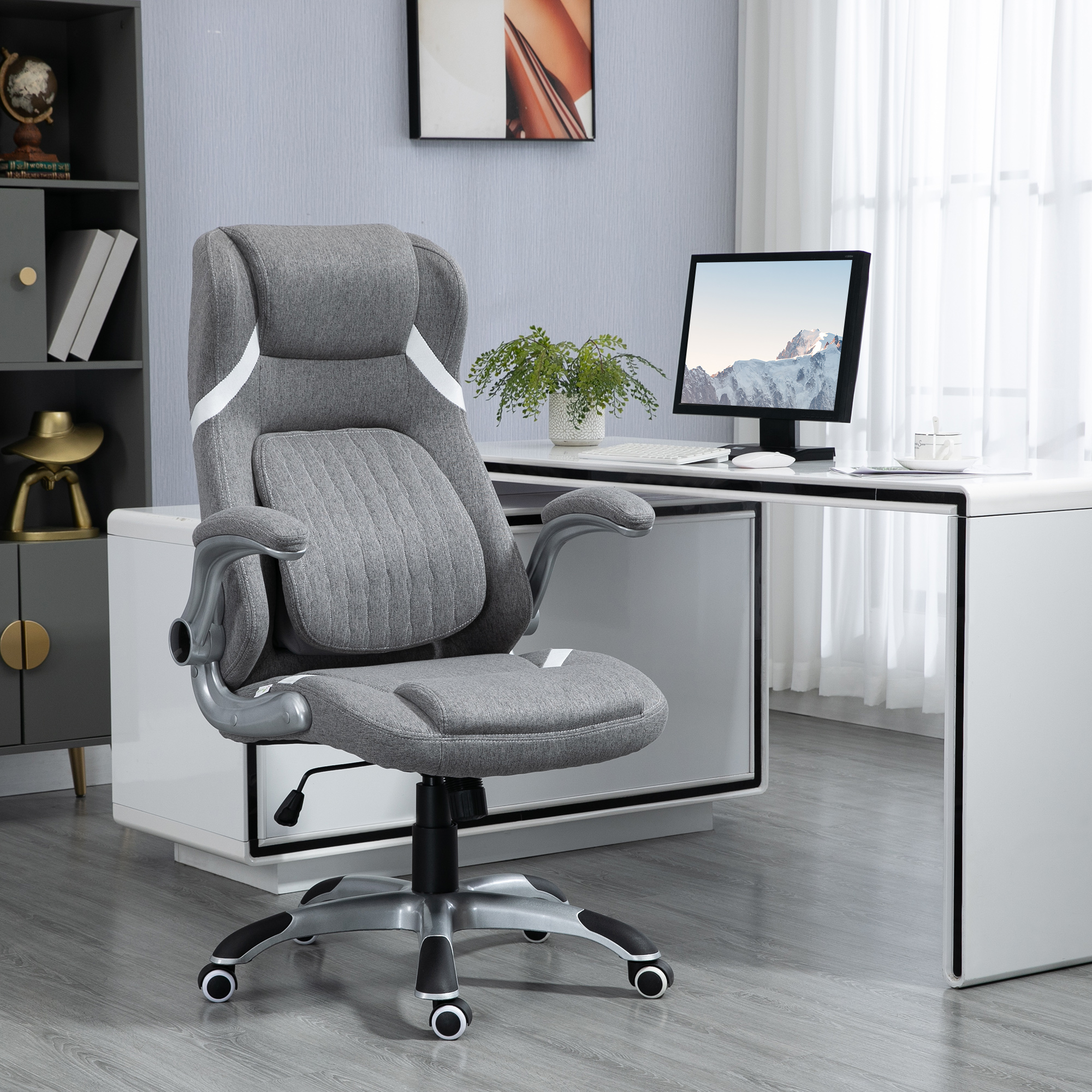 Una sedia da ufficio ergonomica grigia con dettagli bianchi davanti a una scrivania bianca e computer.