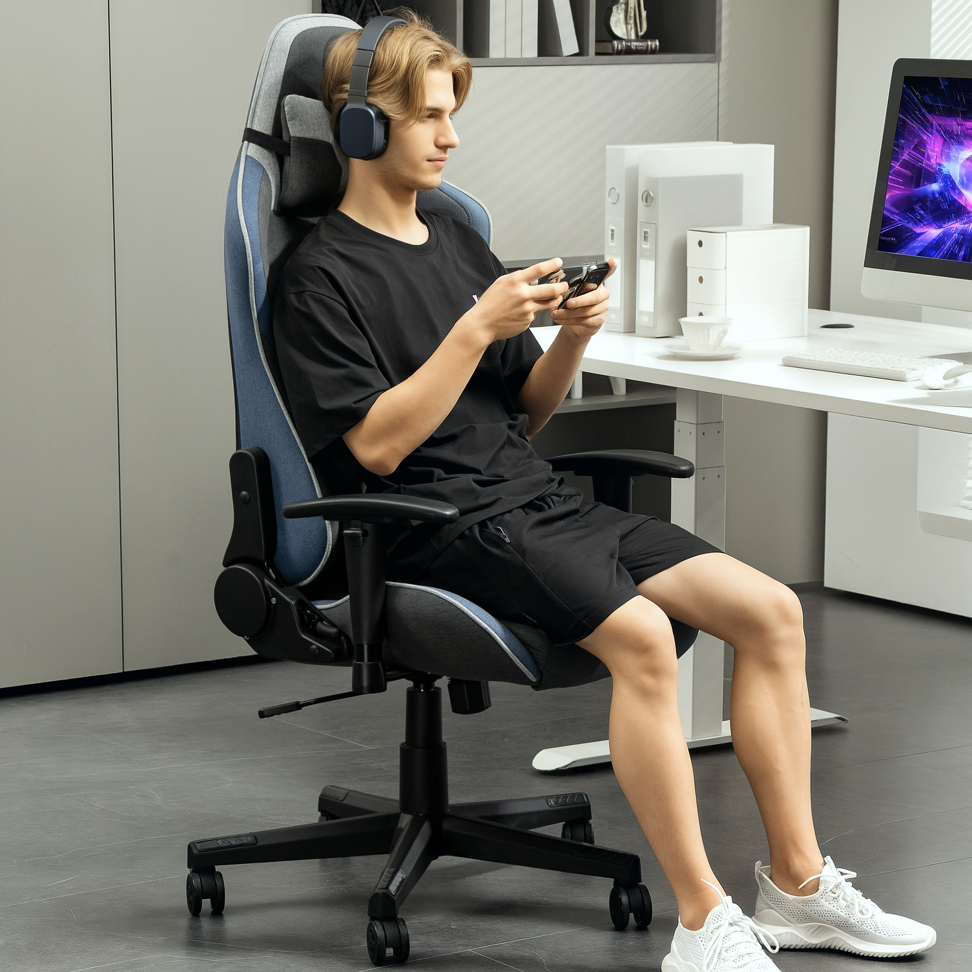 Un giovane con le cuffie siede su una sedia da gioco blu, tenendo un controller in un ufficio.