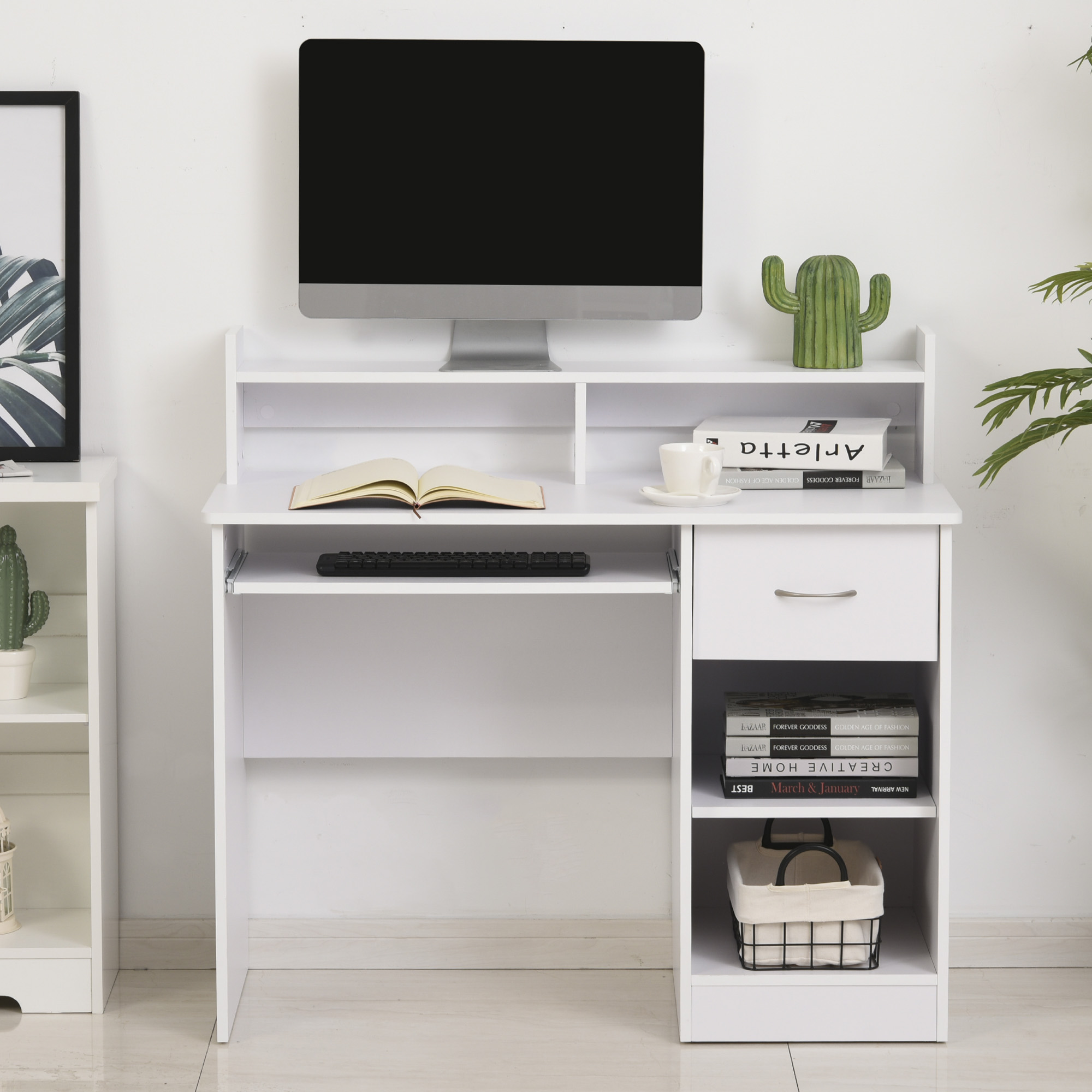 Una scrivania bianca con monitor, tastiera, libri, tazza e decorazioni contro una parete bianca.