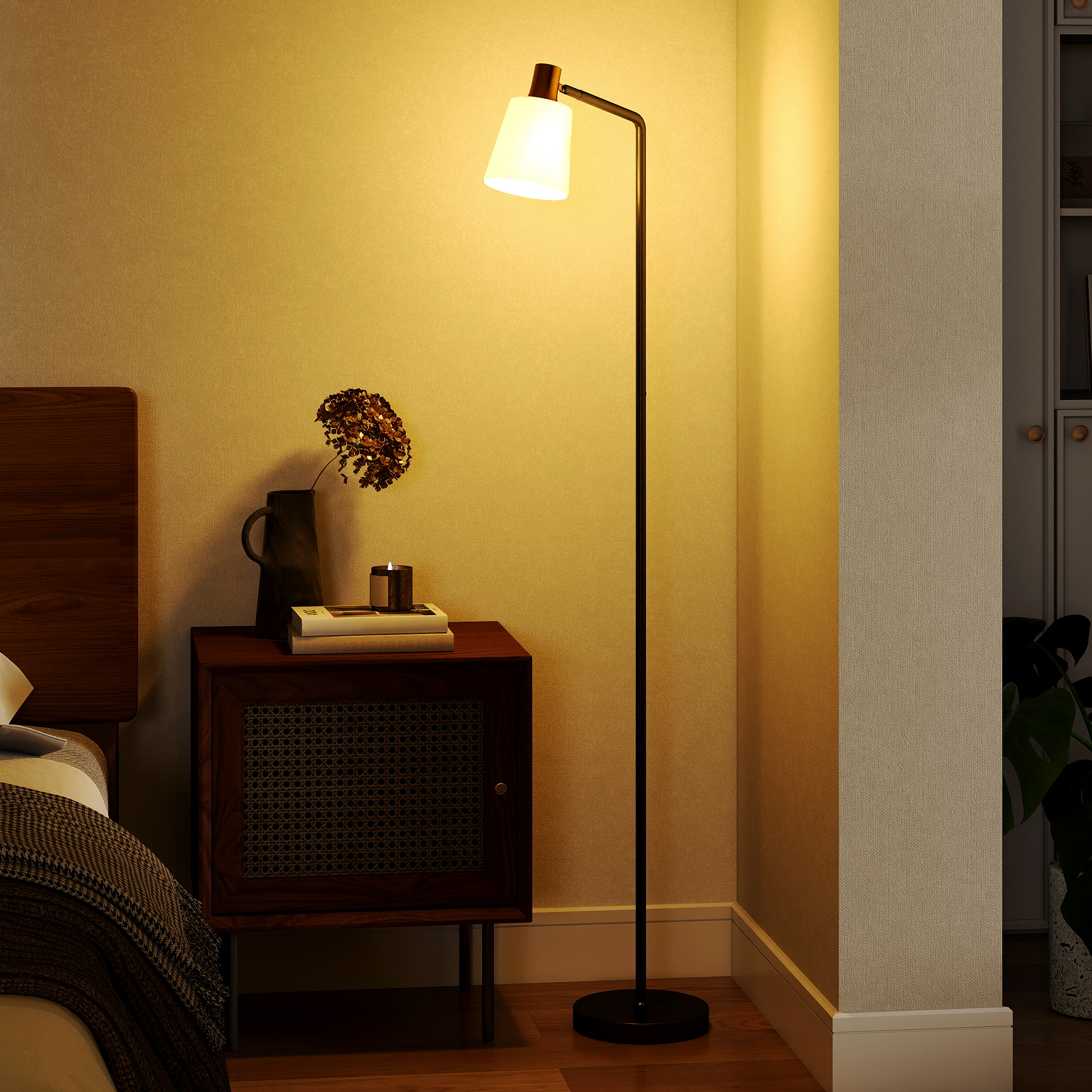 Una sottile lampada da terra brilla calda accanto a un comodino in legno con vaso e libri.