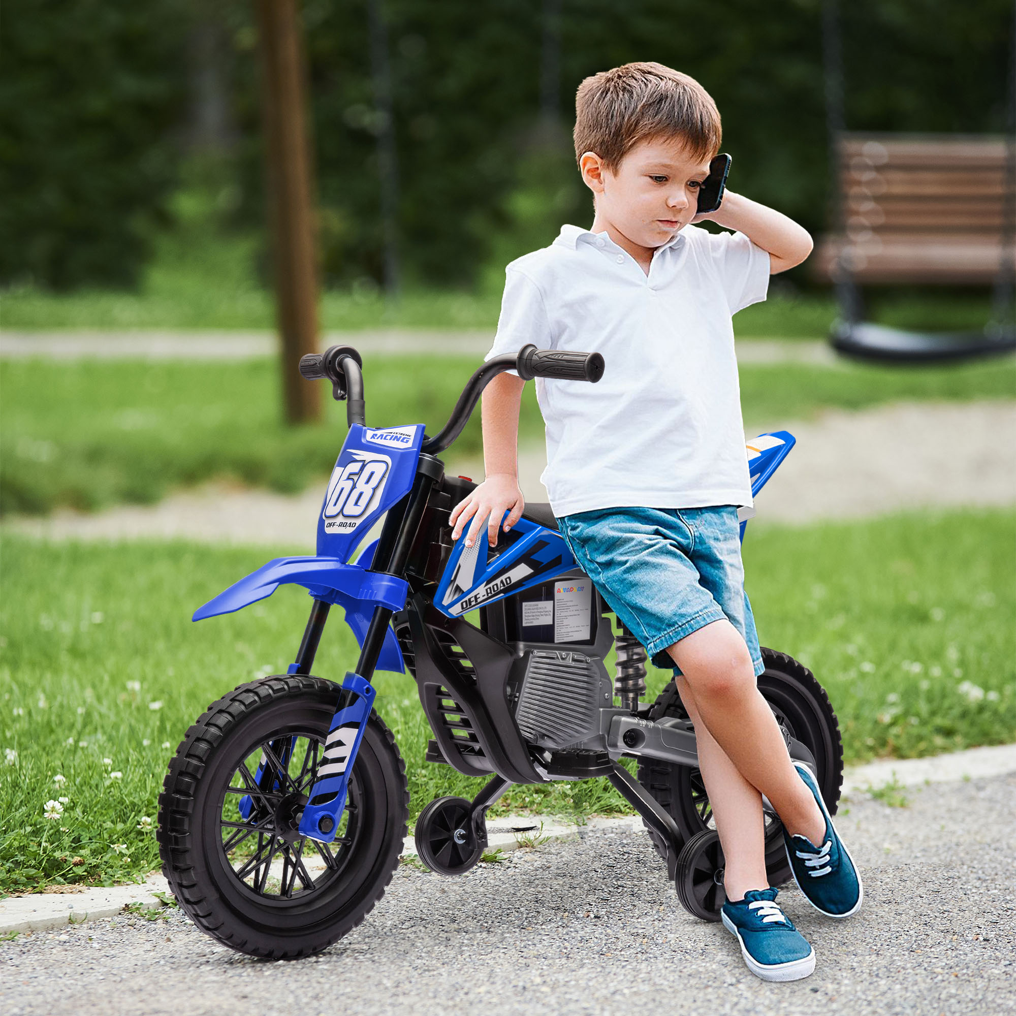 Un ragazzo con camicia bianca e pantaloncini blu parla al telefono vicino a una moto giocattolo blu all'aperto.