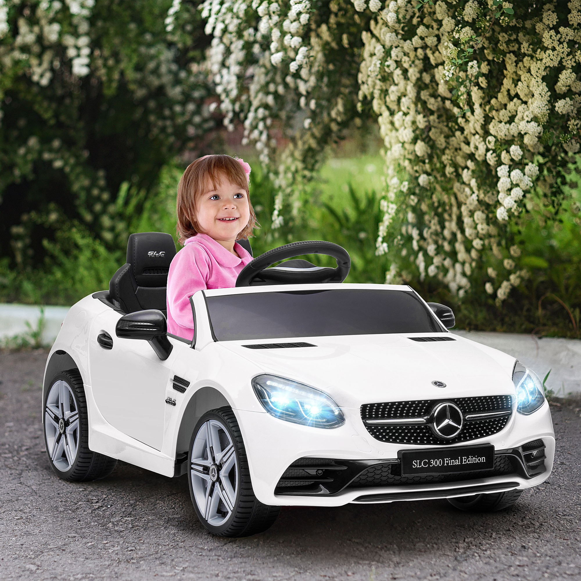 Bambina con top rosa seduta su un'auto giocattolo elettrica bianca davanti a fiori bianchi.