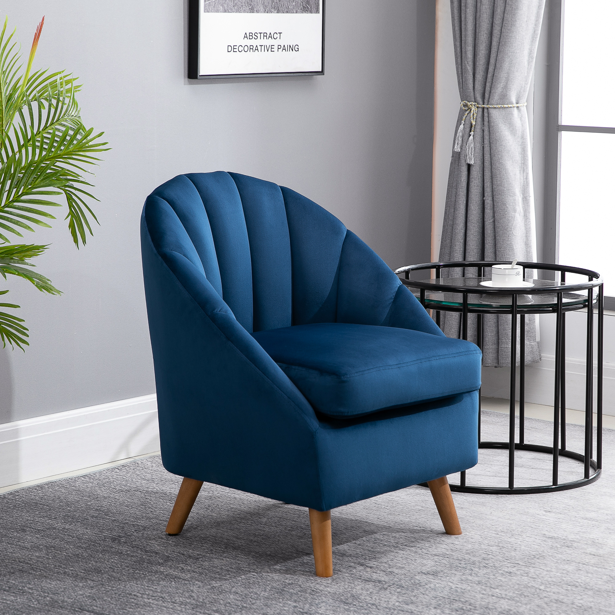 Poltrona in velluto blu con gambe in legno in una stanza grigia.