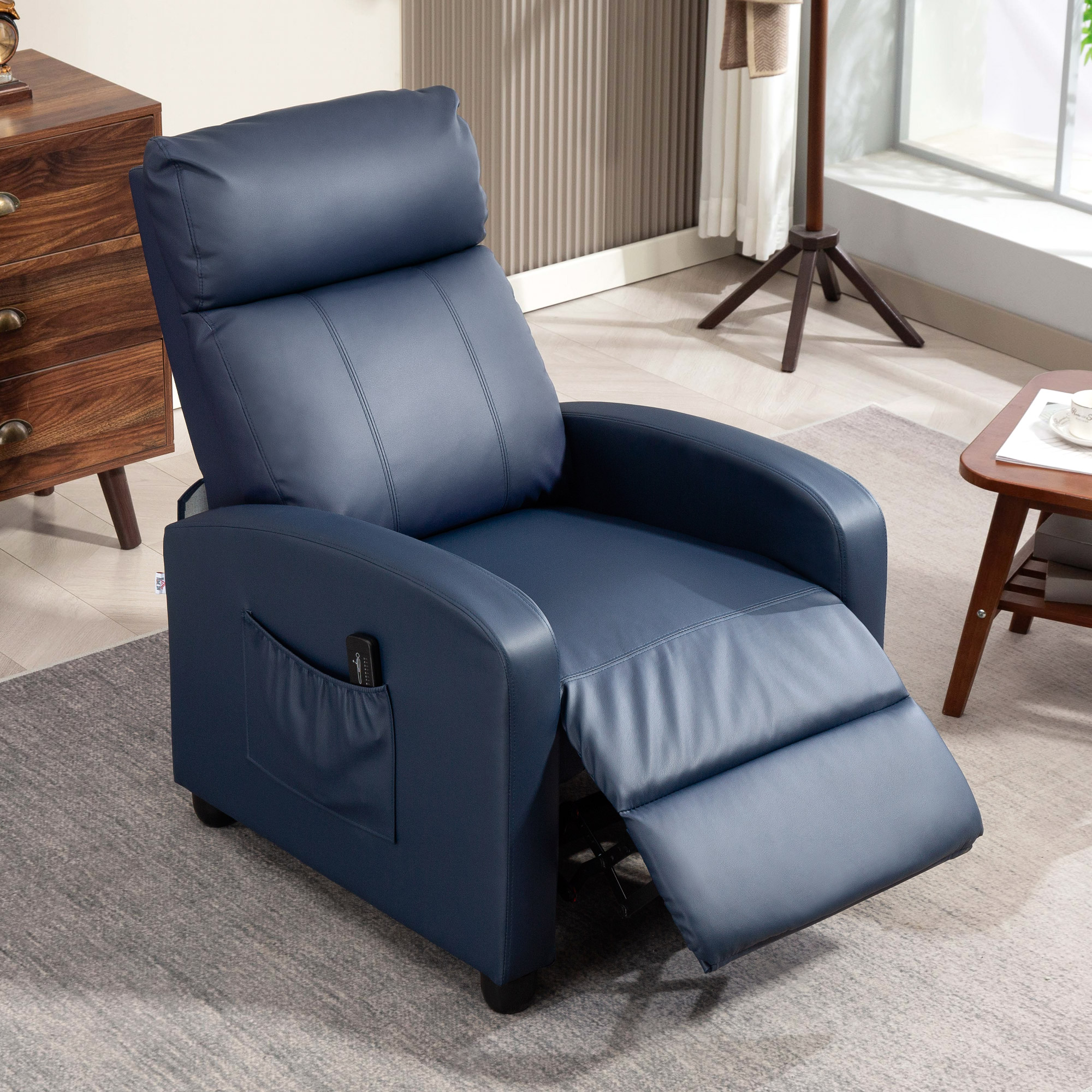 Una moderna poltrona in pelle blu scuro con poggiapiedi si trova su un tappeto grigio in una stanza luminosa.