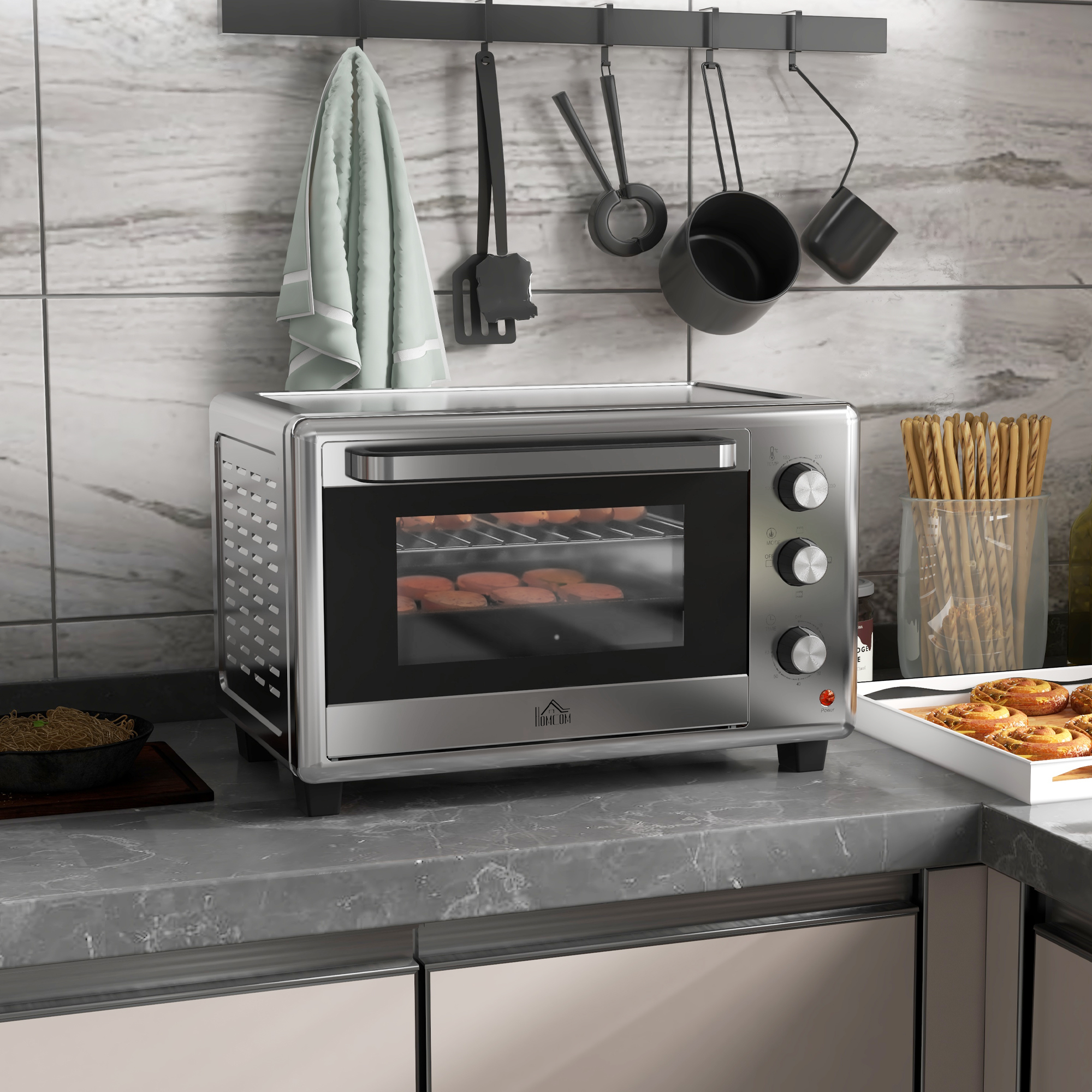Mini forno argentato su un piano di marmo in una cucina moderna con utensili appesi.