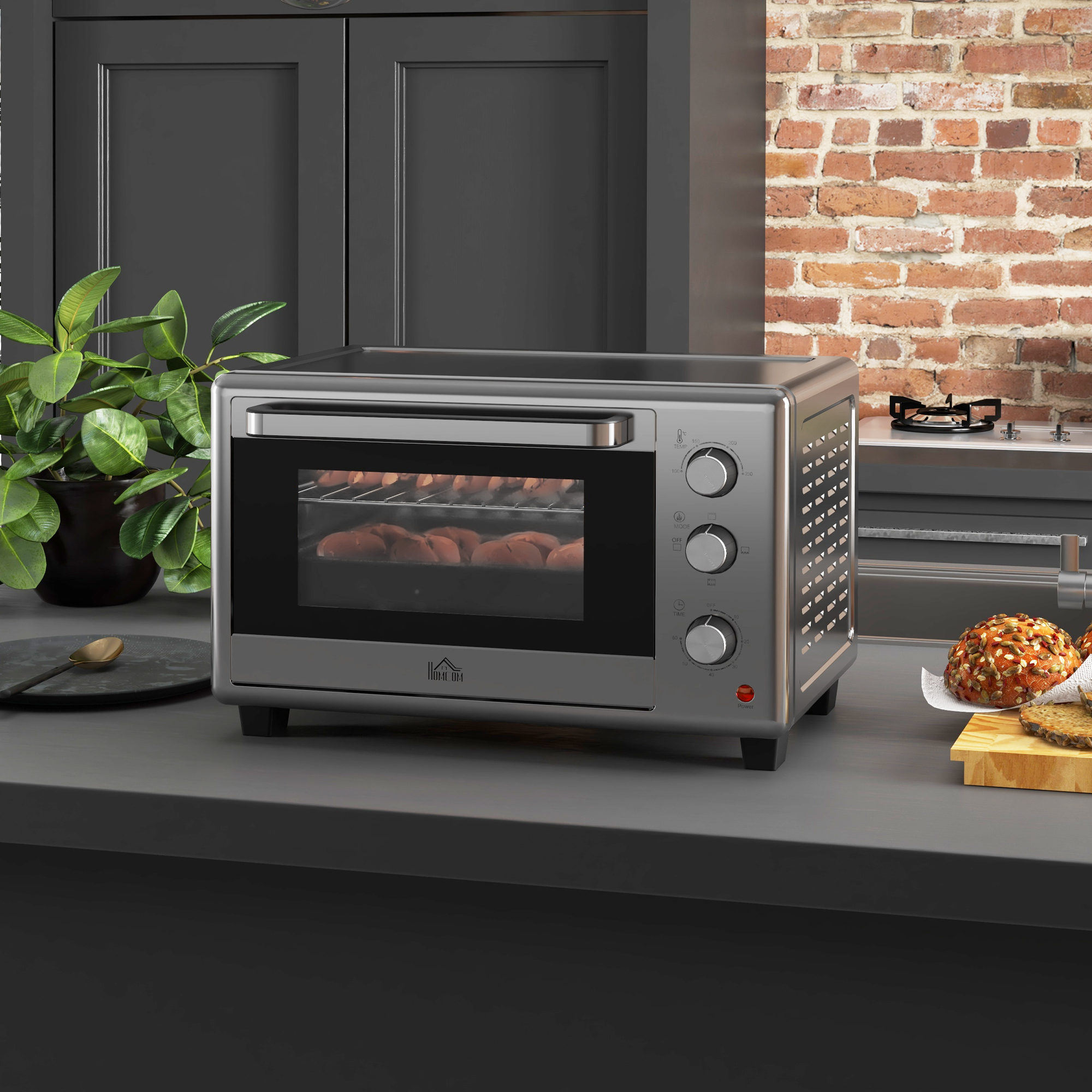 Un mini forno argentato su un piano di lavoro grigio in una cucina con parete in mattoni rossi.