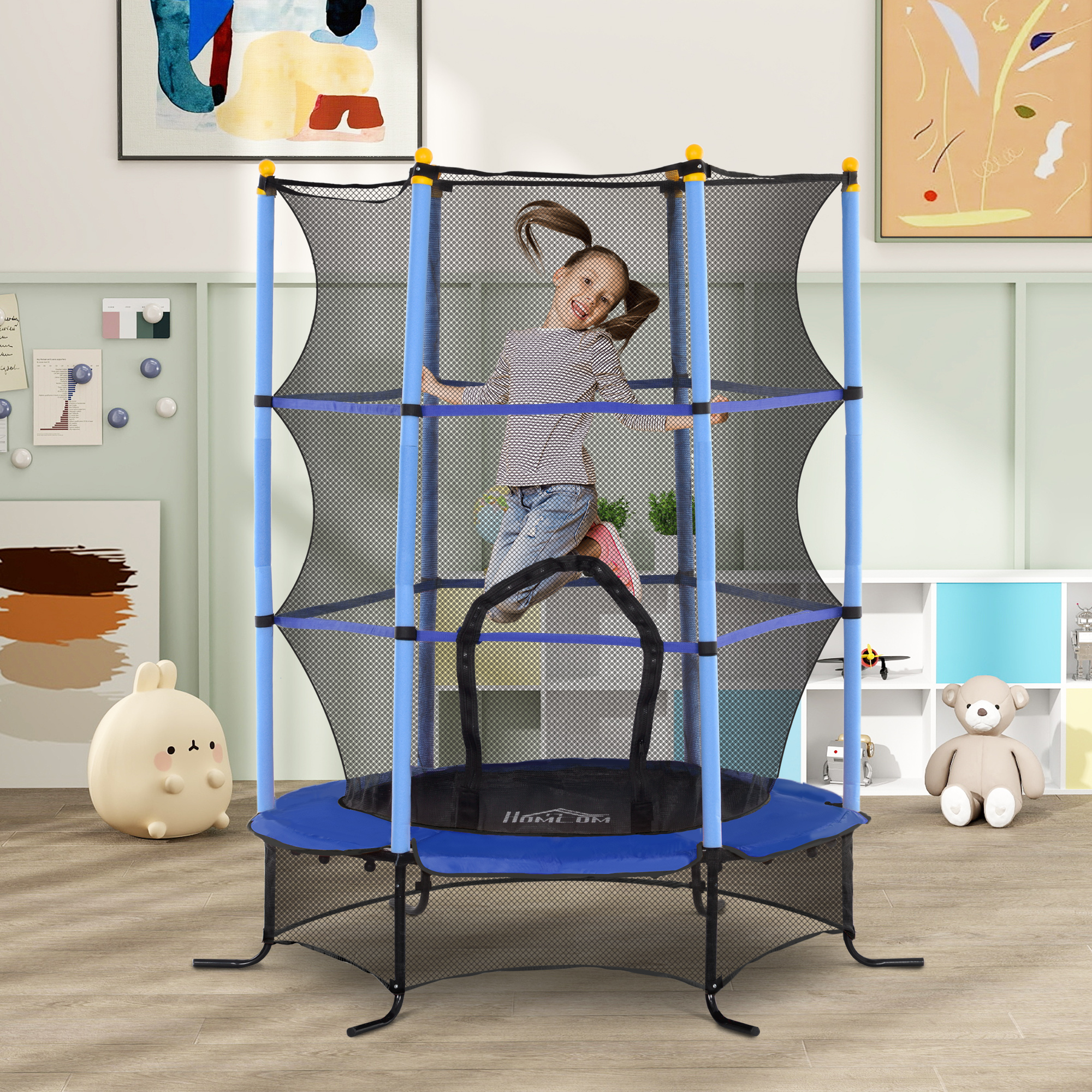 Una bambina con le treccine salta gioiosamente su un tappeto elastico blu da interno con rete.