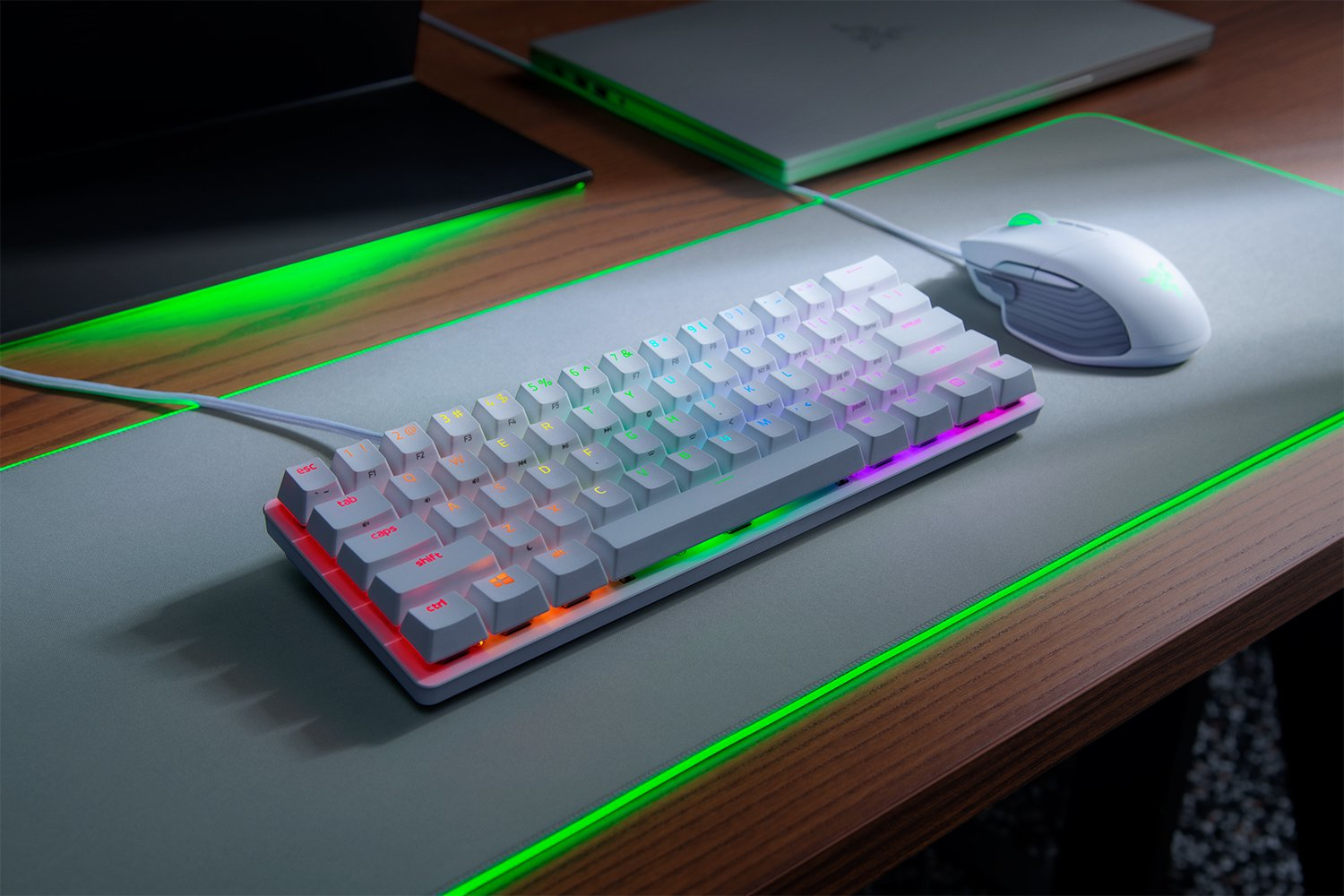 Eine weiße Gaming-Tastatur und Maus liegen auf einem grün beleuchteten Mauspad auf einem Holzschreibtisch.