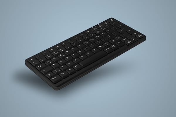 Un teclado inalambrico negro inclinado sobre un fondo gris liso.