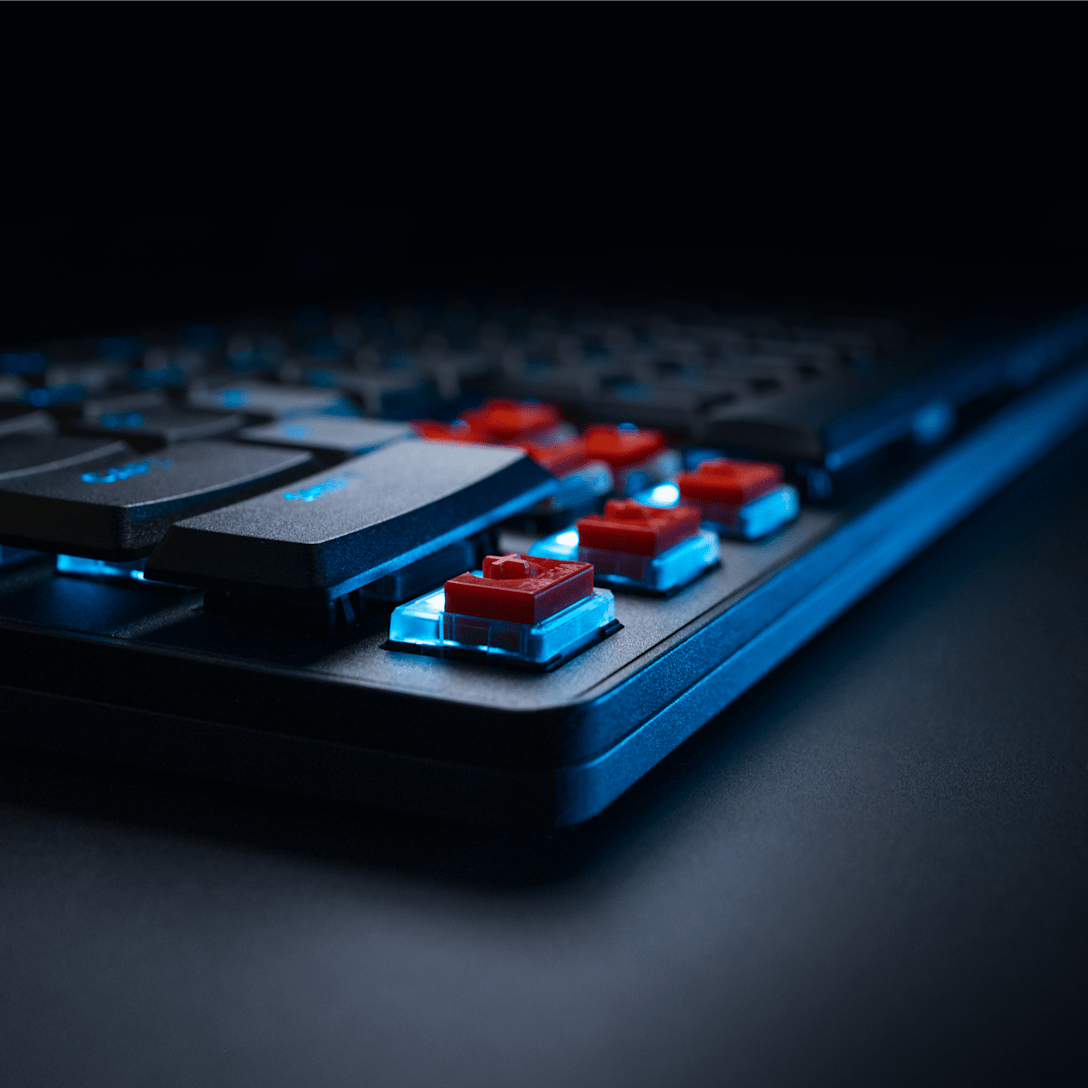 Un teclado mecánico con retroiluminación azul e interruptores rojos expuestos sobre un fondo oscuro.