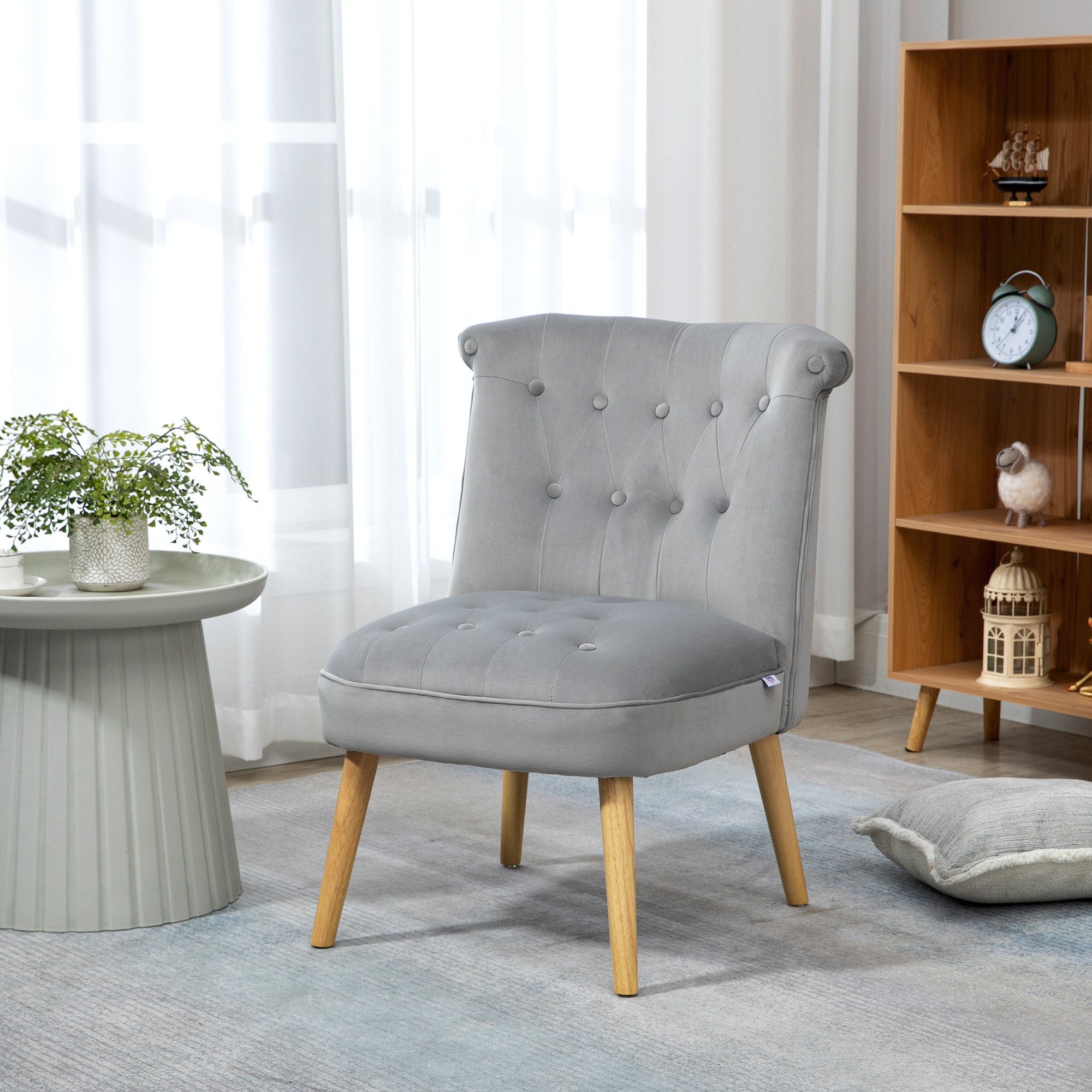 Una poltrona imbottita grigia con gambe in legno in una stanza luminosa con tavolo e libreria.
