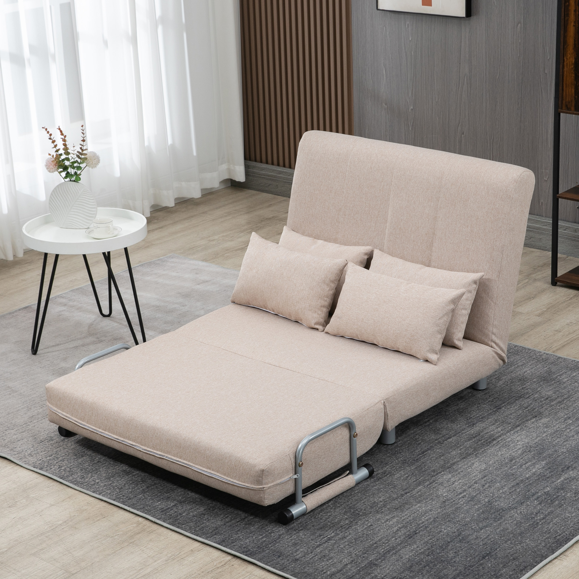 Un divano letto beige con cuscini su un tappeto grigio in una stanza con parete in legno.