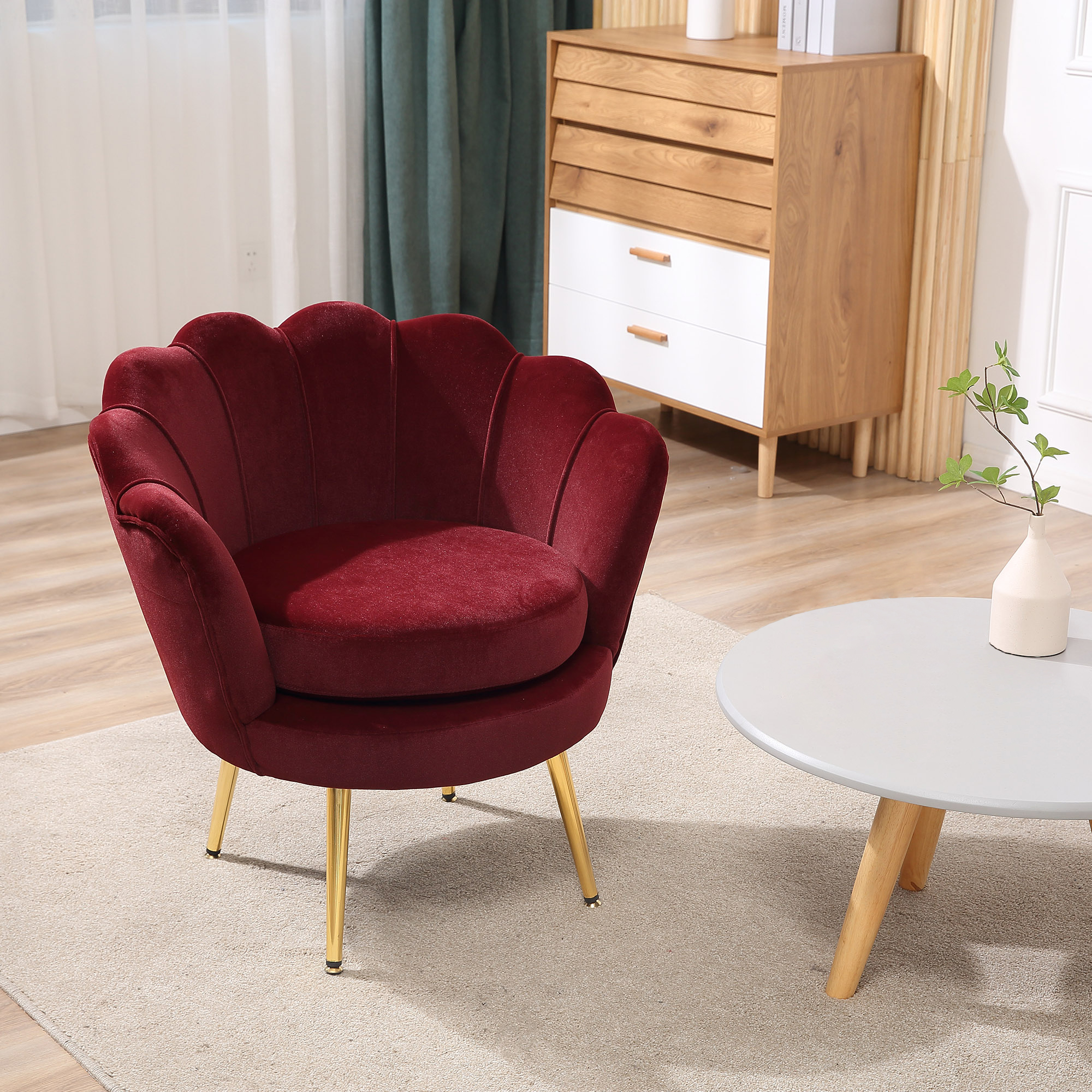 Una poltrona in velluto rosso con gambe dorate si trova in una stanza luminosa accanto a un tavolo rotondo.