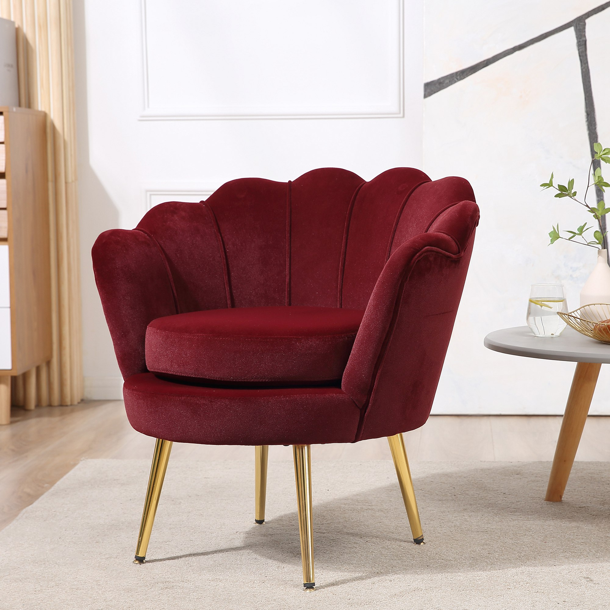 Una poltrona in velluto bordeaux con schienale a conchiglia e gambe dorate su un tappeto chiaro in una stanza luminosa.
