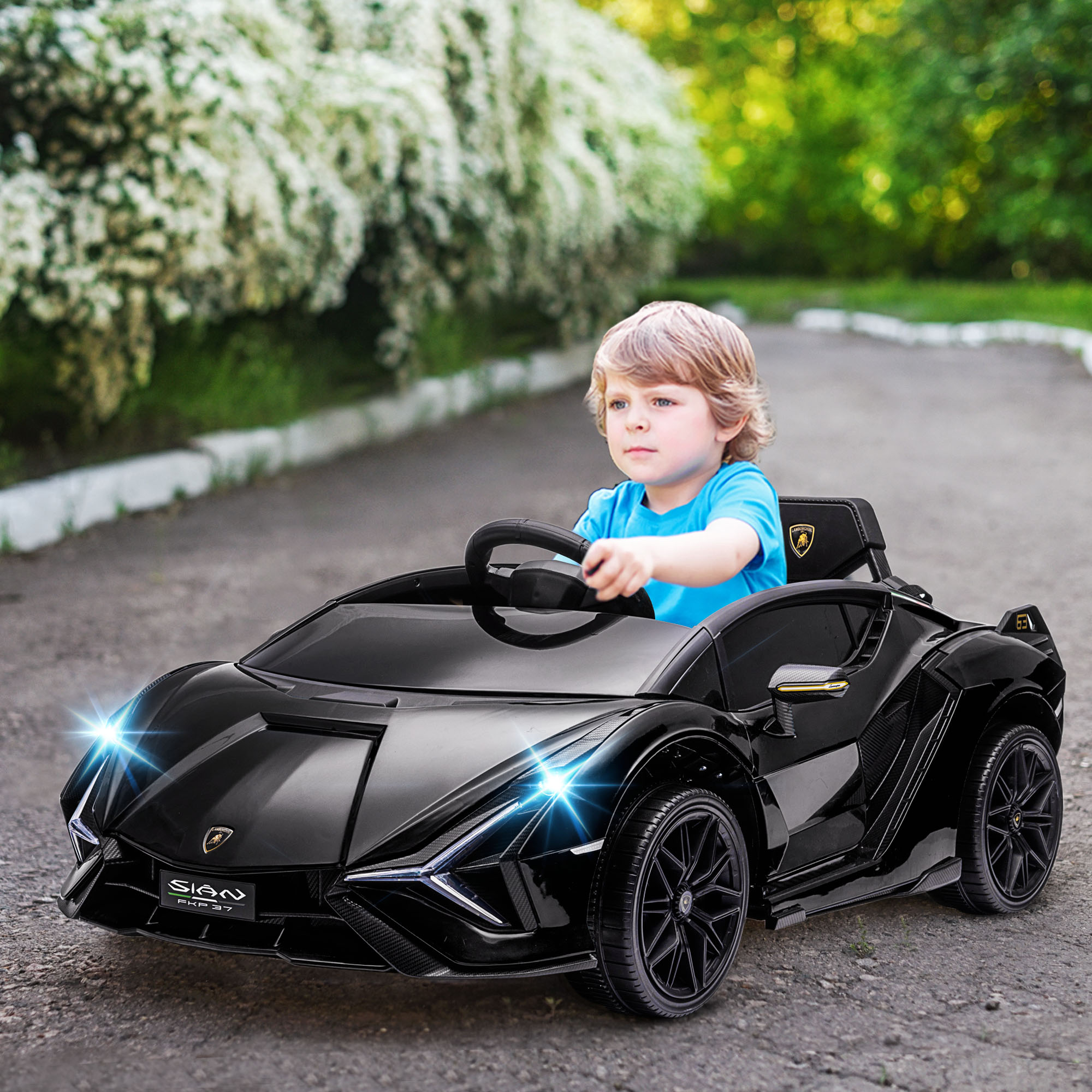 Un giovane ragazzo in camicia blu guida una Lamborghini giocattolo nera su un sentiero asfaltato.