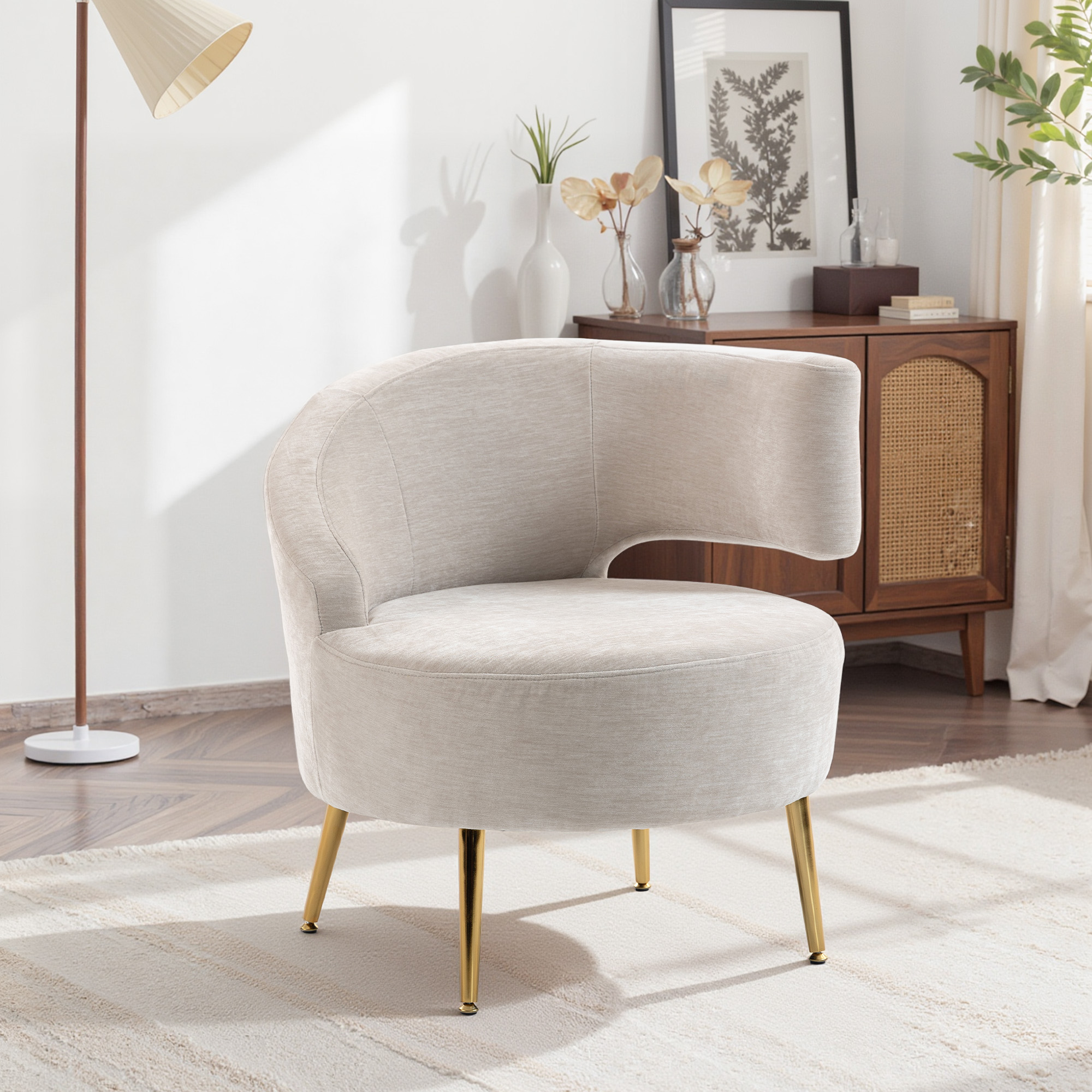 Una poltrona color crema con gambe dorate si trova in una stanza luminosa davanti a una credenza in legno.