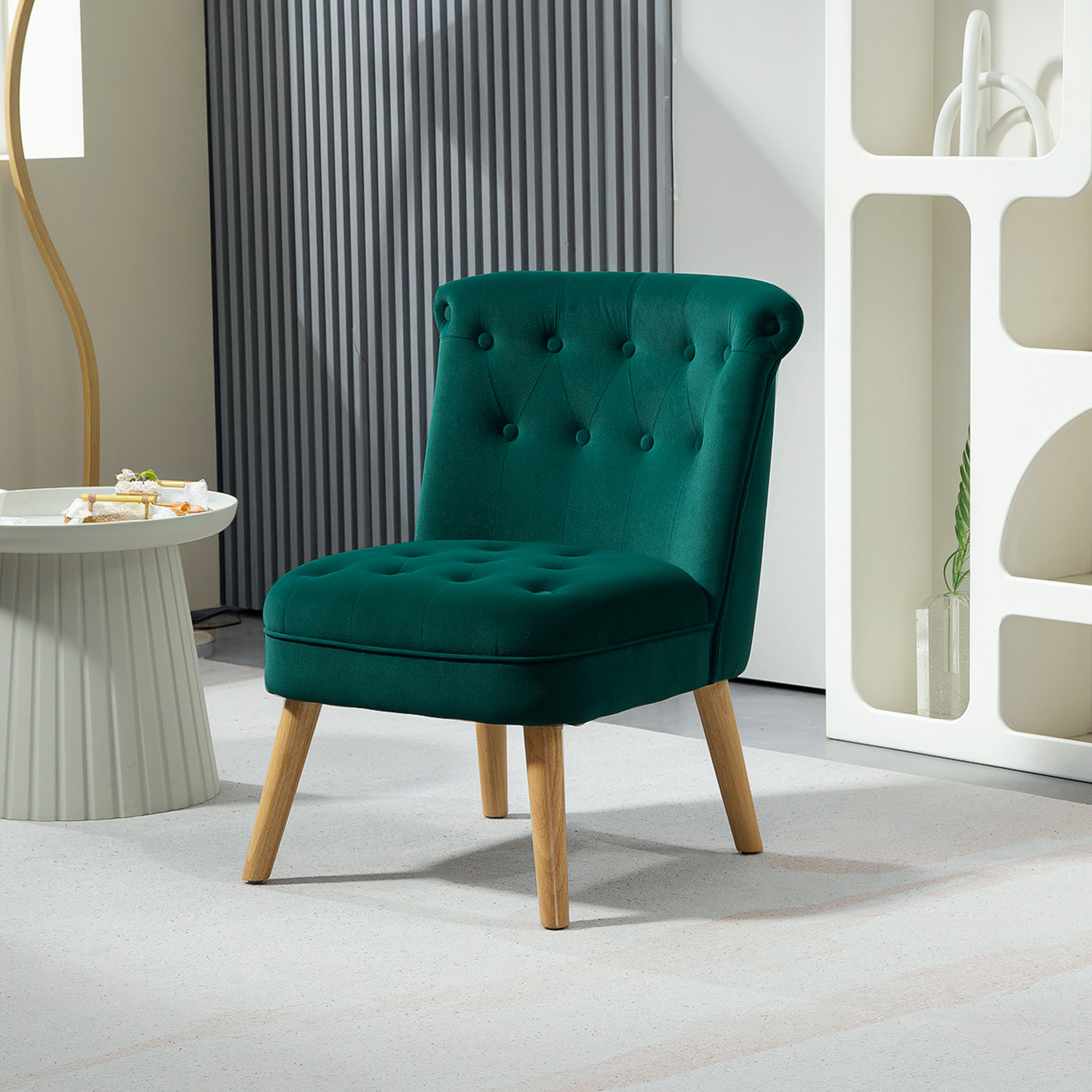 Una poltrona in velluto verde trapuntato con gambe in legno chiaro su un tappeto bianco, accanto a un tavolino.