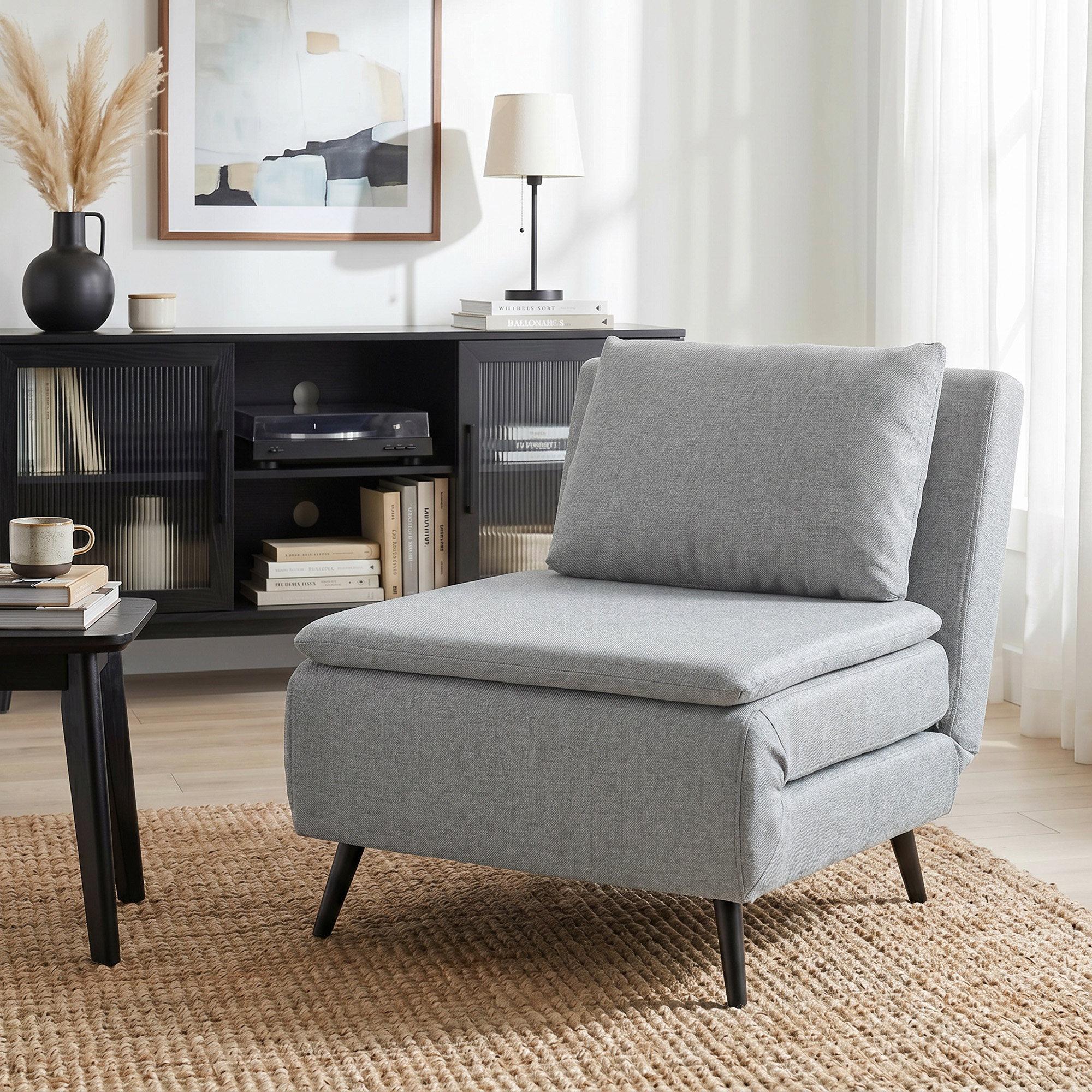 Una poltrona grigia su un tappeto di juta, con una credenza nera, lampada e opera d'arte sullo sfondo.