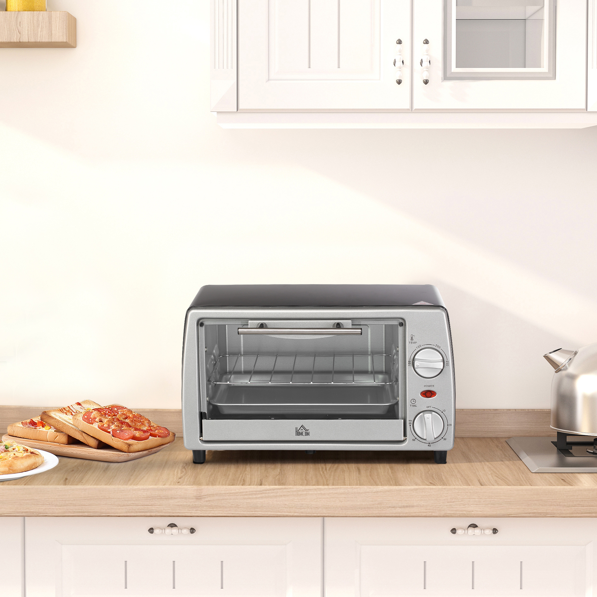Un mini forno argentato su un piano di lavoro in legno in una cucina bianca, con toast e un bollitore.