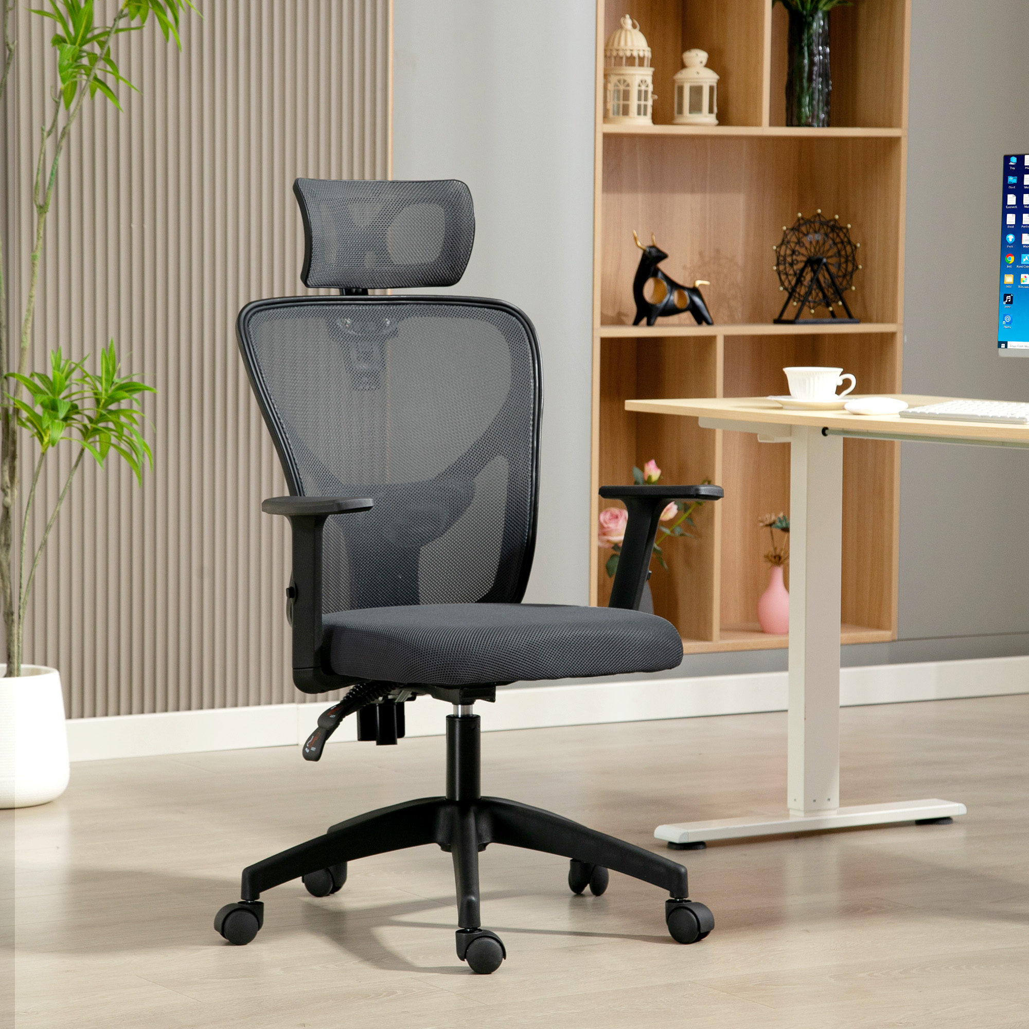 Una sedia da ufficio ergonomica grigia con rotelle si trova in un ufficio moderno davanti a uno scaffale e a una scrivania in legno.
