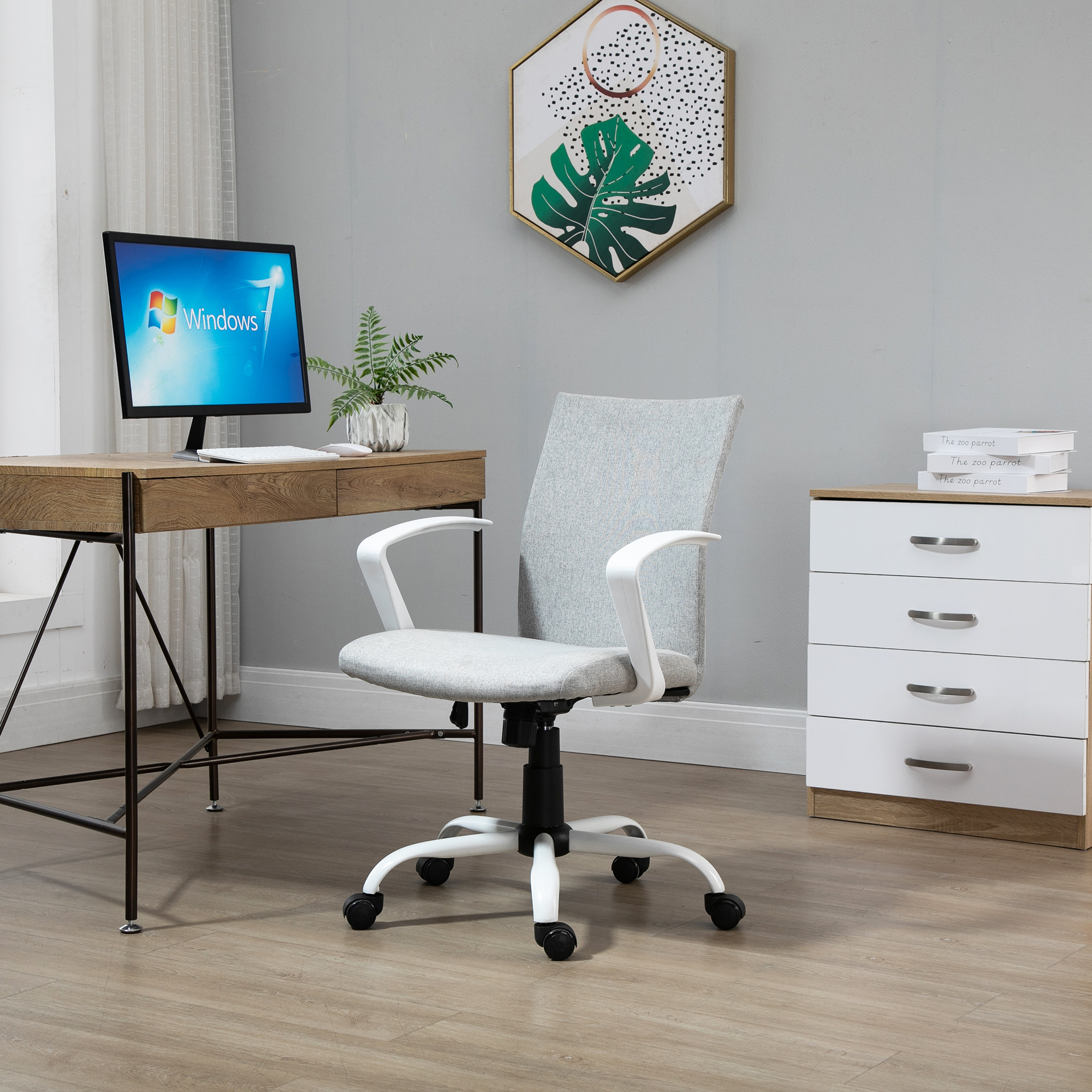 Una moderna scrivania con sedia, monitor e libri impilati contro una parete grigia.