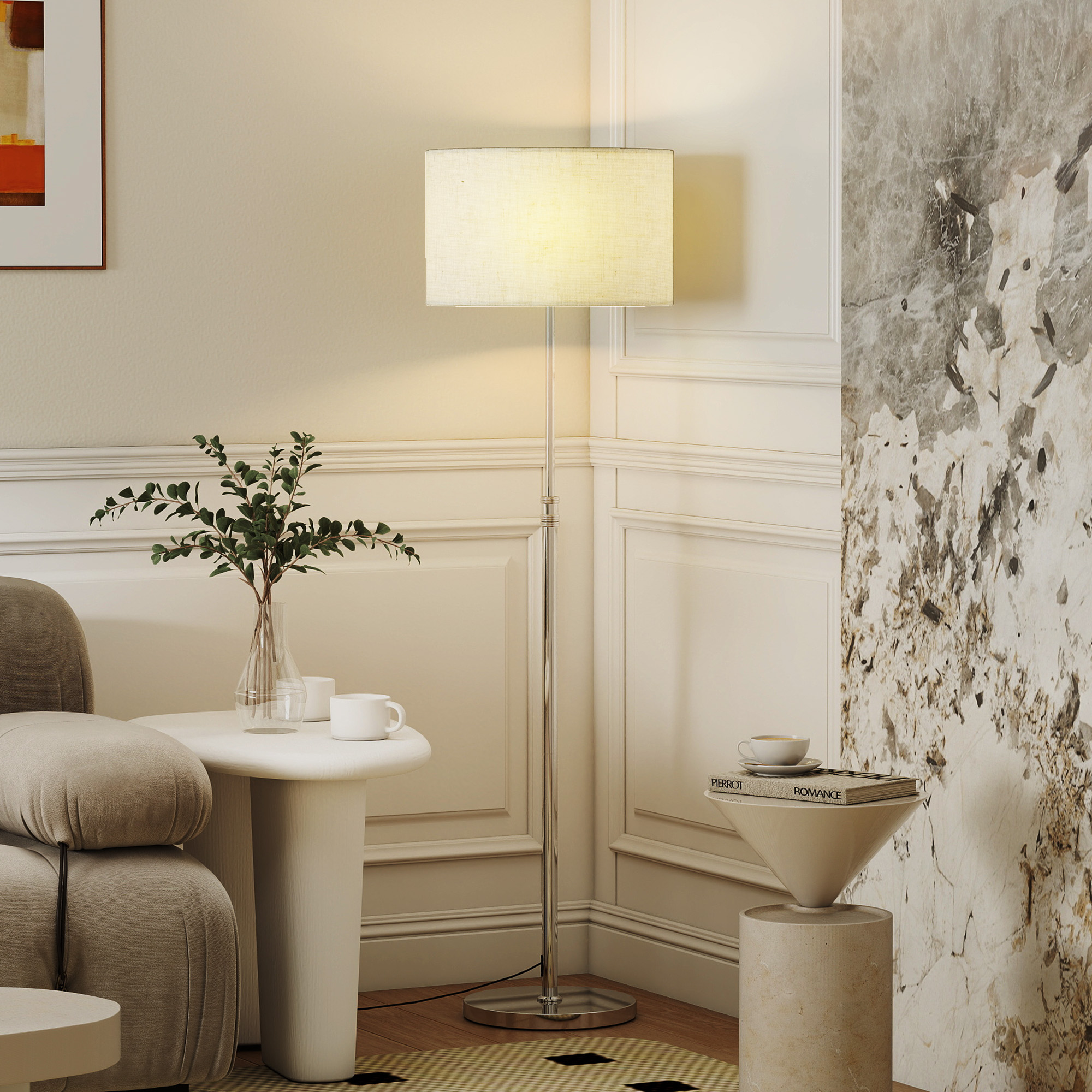 Una piantana illumina un angolo con un divano chiaro, piccoli tavoli e una parete artistica.
