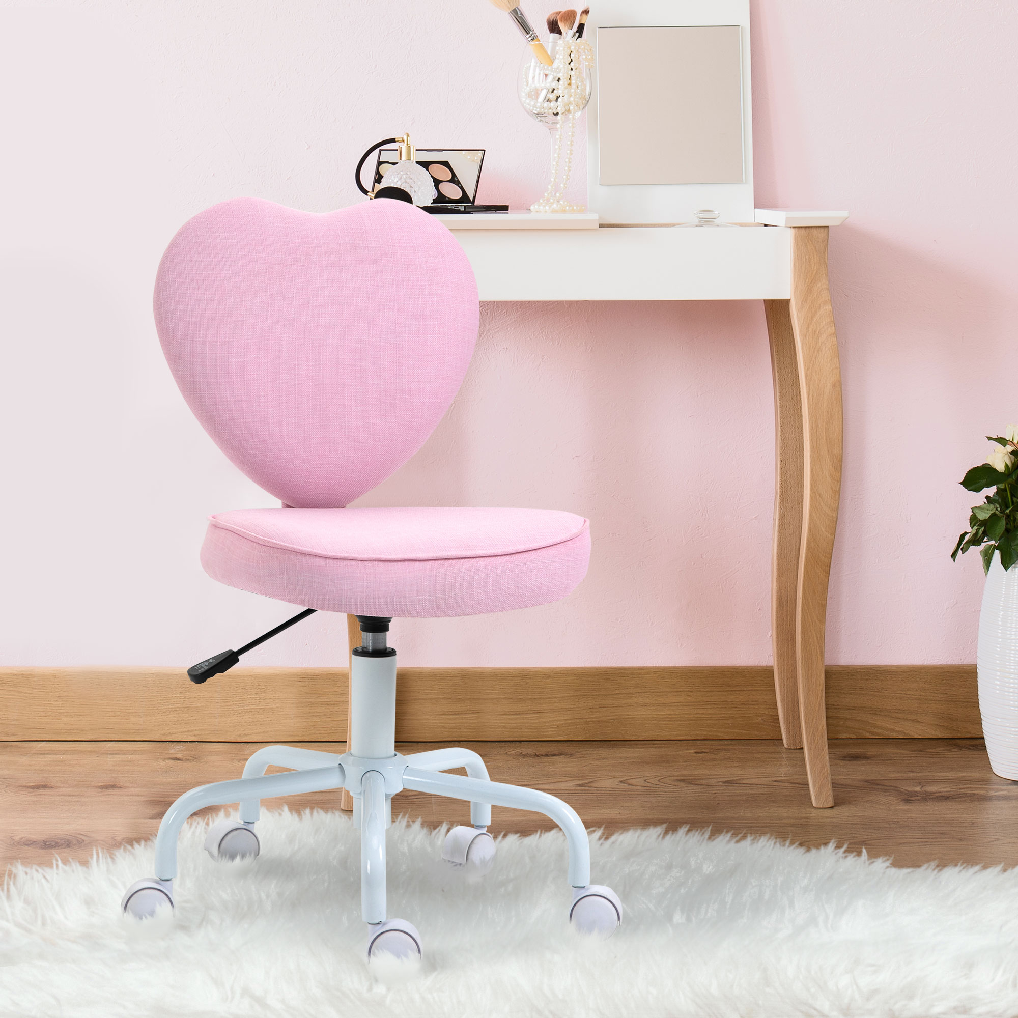 Una sedia da ufficio rosa a forma di cuore con ruote davanti a un tavolo da toeletta bianco.