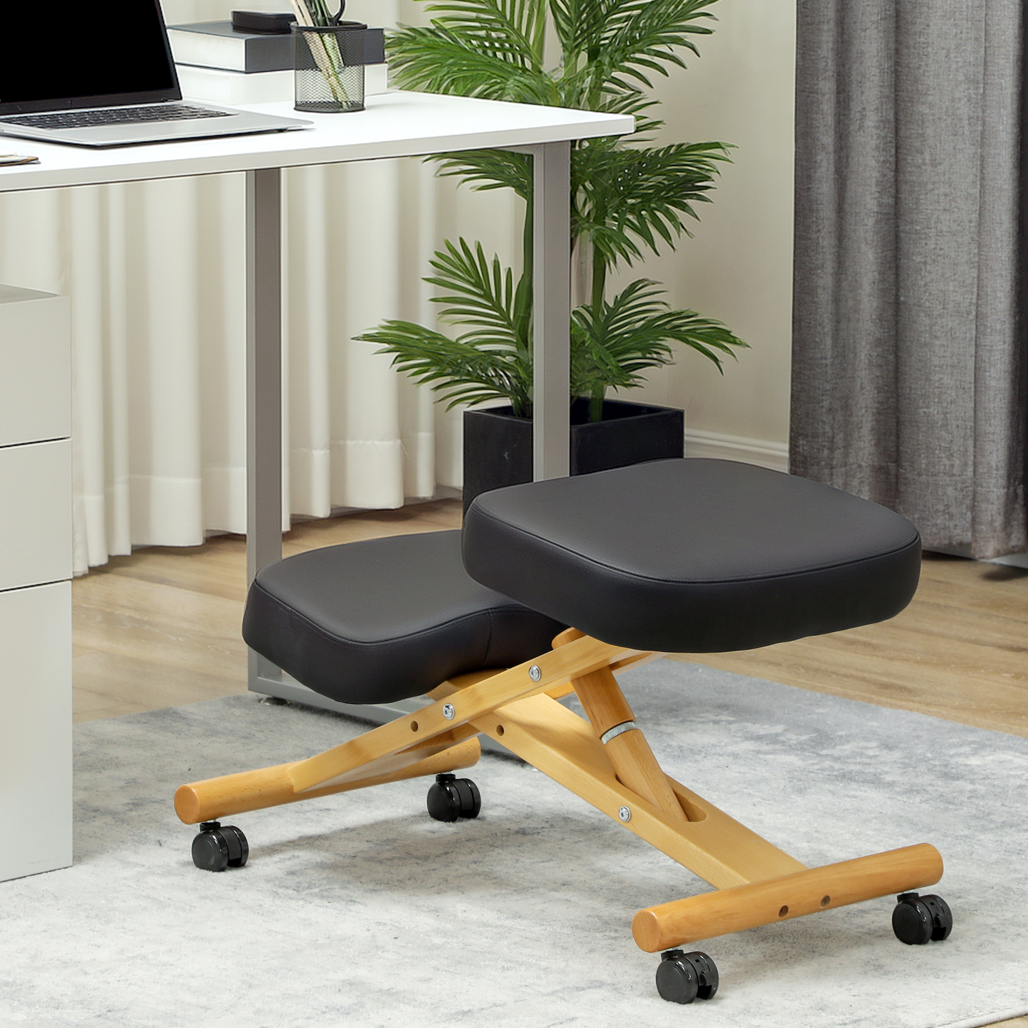 Una sedia ergonomica in ginocchio con struttura in legno e cuscini neri su ruote si trova su un tappeto grigio davanti a una scrivania.