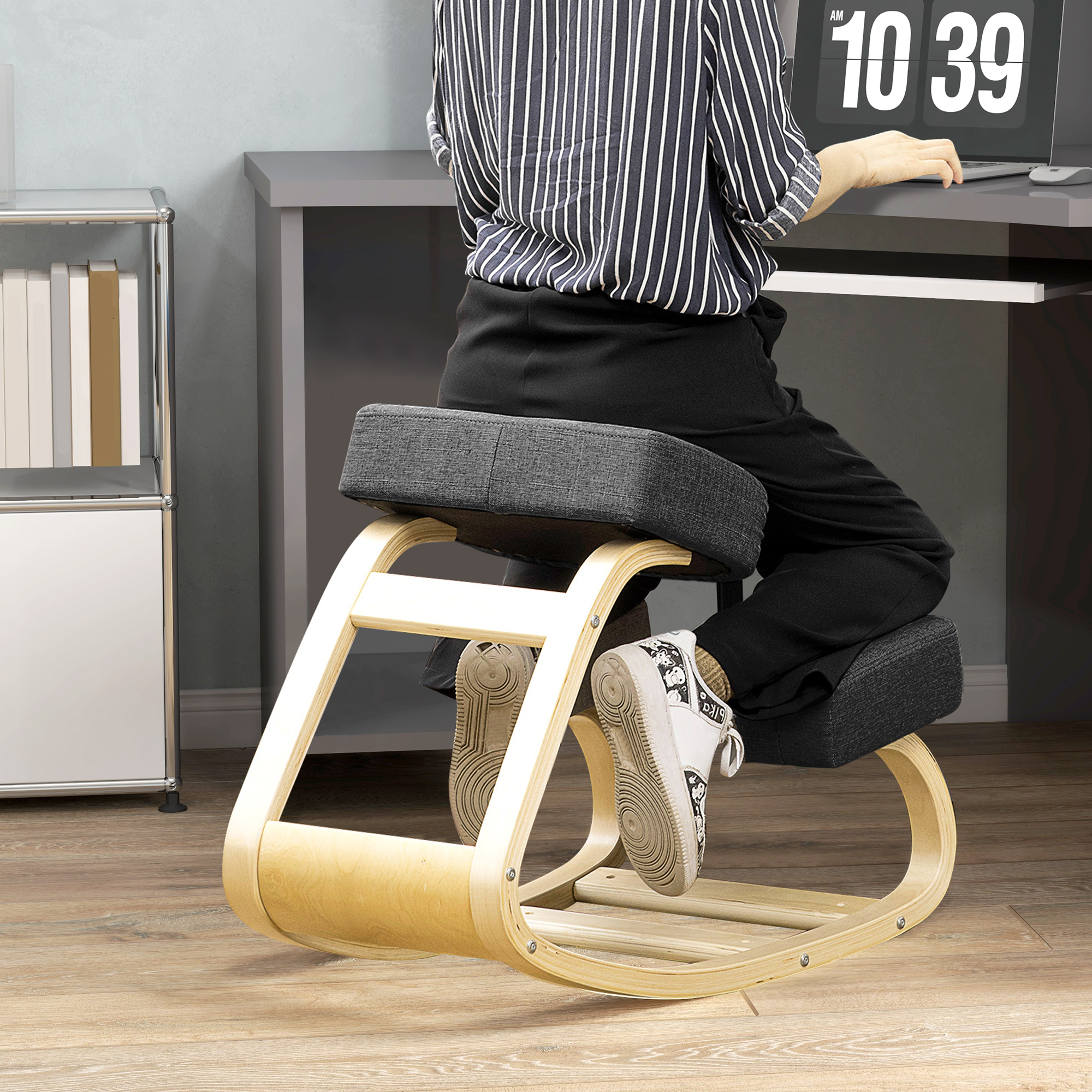 Persona lavora a una scrivania seduta su una sedia ergonomica per ginocchia con struttura in legno e cuscini grigi.
