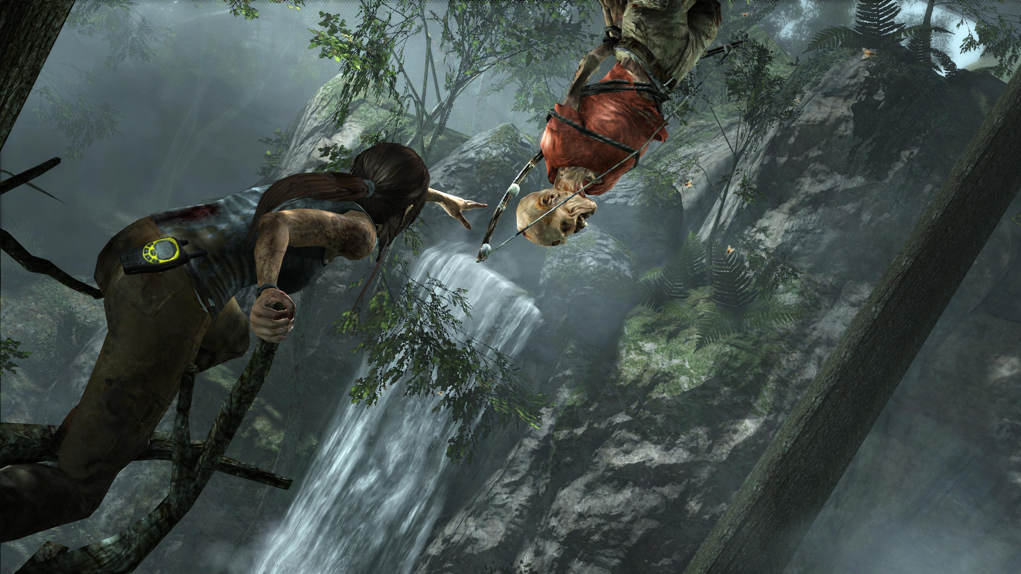 Lara Croft greift auf einem Ast nach einer hängenden, gefesselten Leiche an einem Wasserfall.