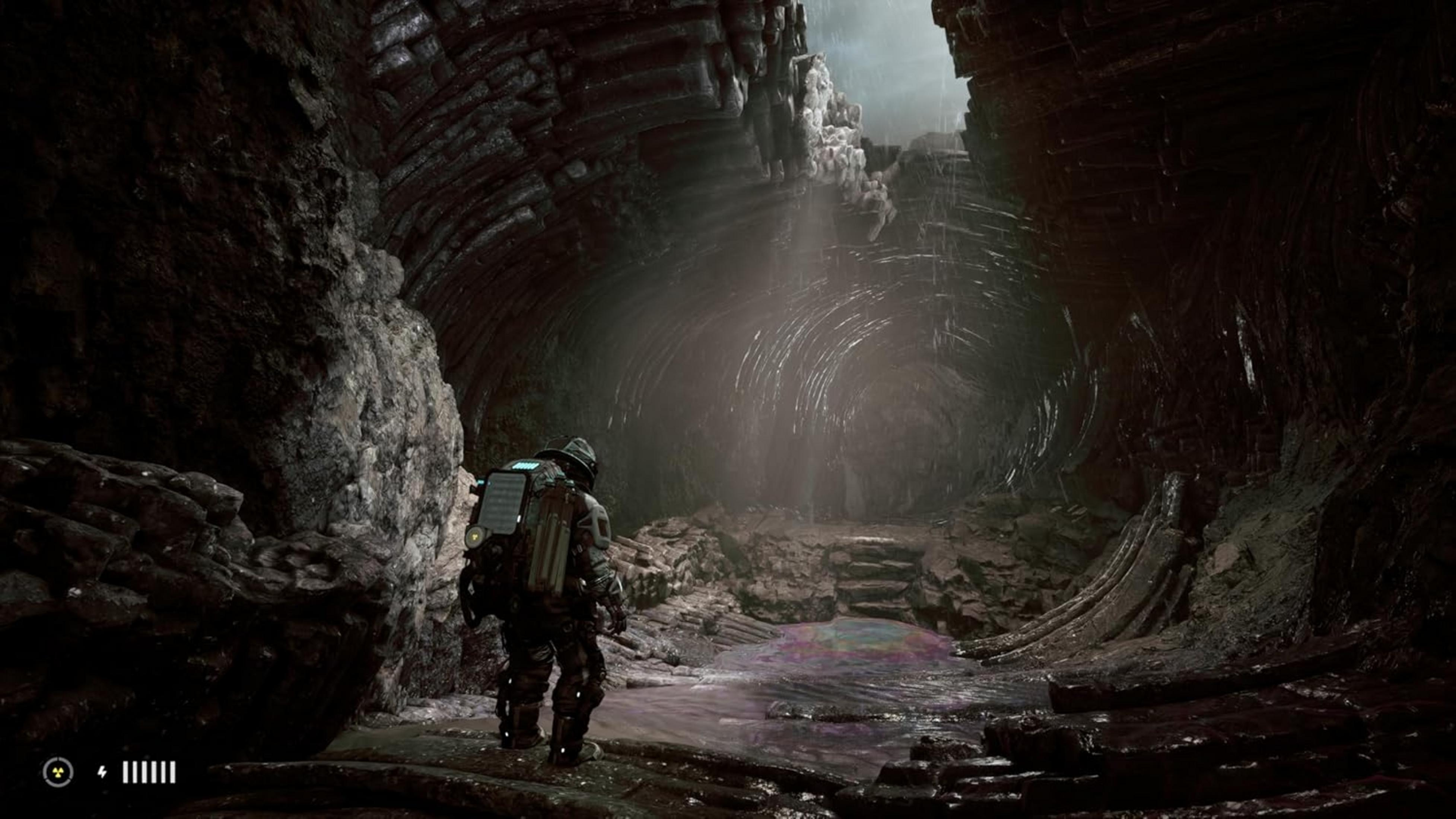 Un astronauta in una grotta buia e rocciosa guarda una pozzanghera d'acqua sotto un fascio di luce.