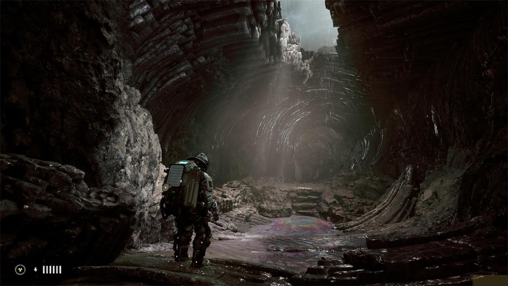 Un astronauta in tuta scura si trova in una grotta buia e rocciosa di fronte a una pozzanghera.